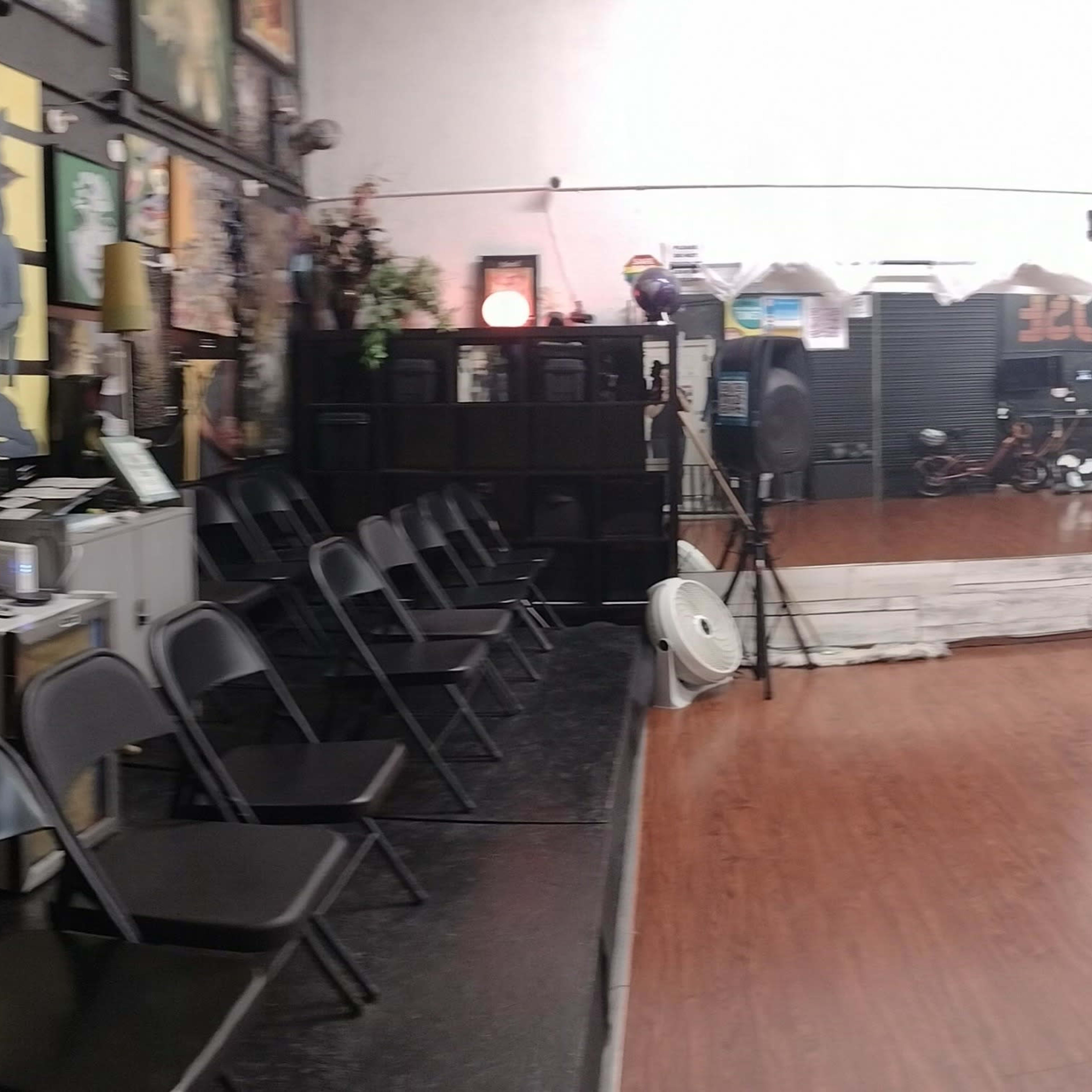 A spacious dance studio featuring a polished wooden floor, floor-to-ceiling mirrors along one wall, and chairs arranged along the side.