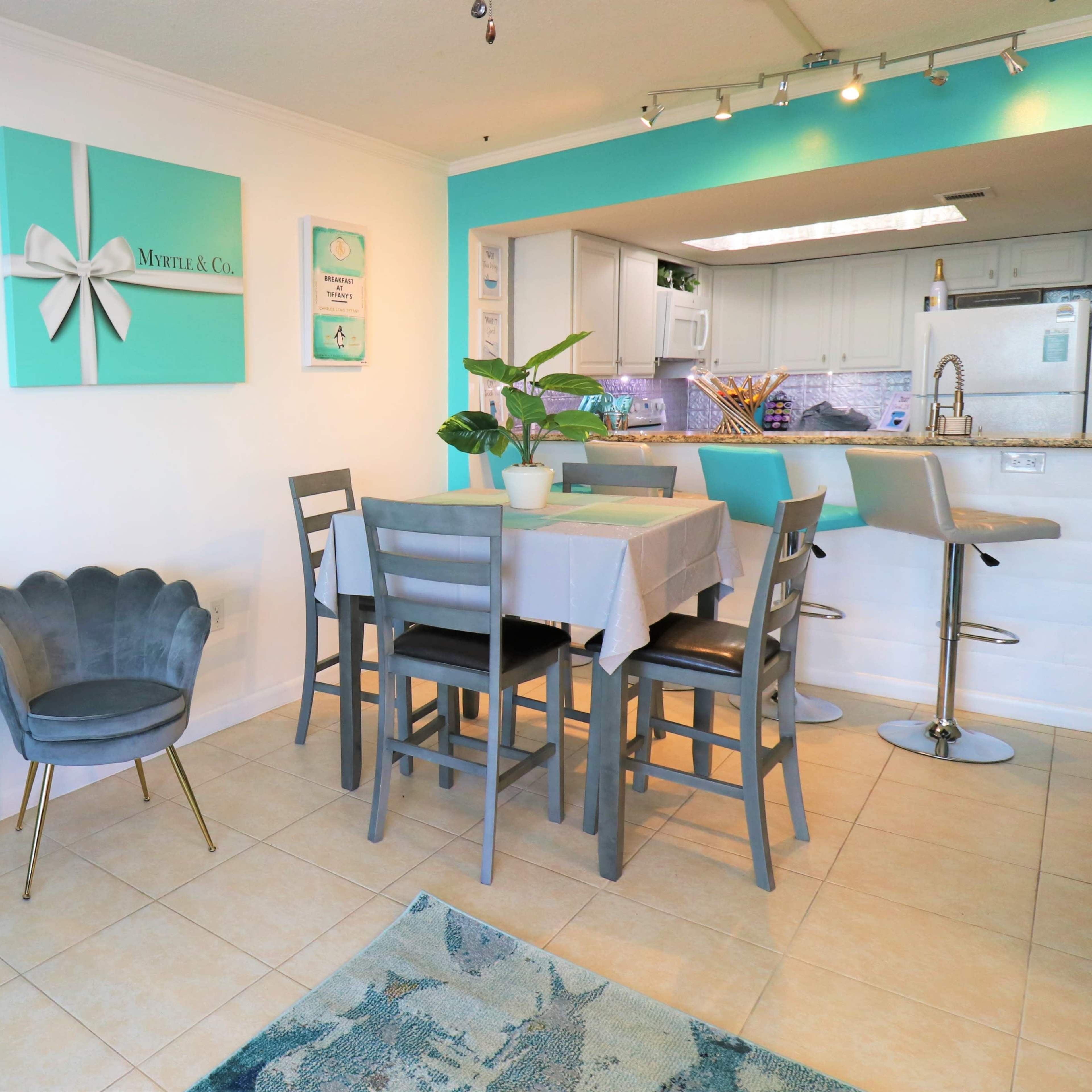 A bright dining area featuring a turquoise-themed decor with a table set for meals and a kitchen in the background.