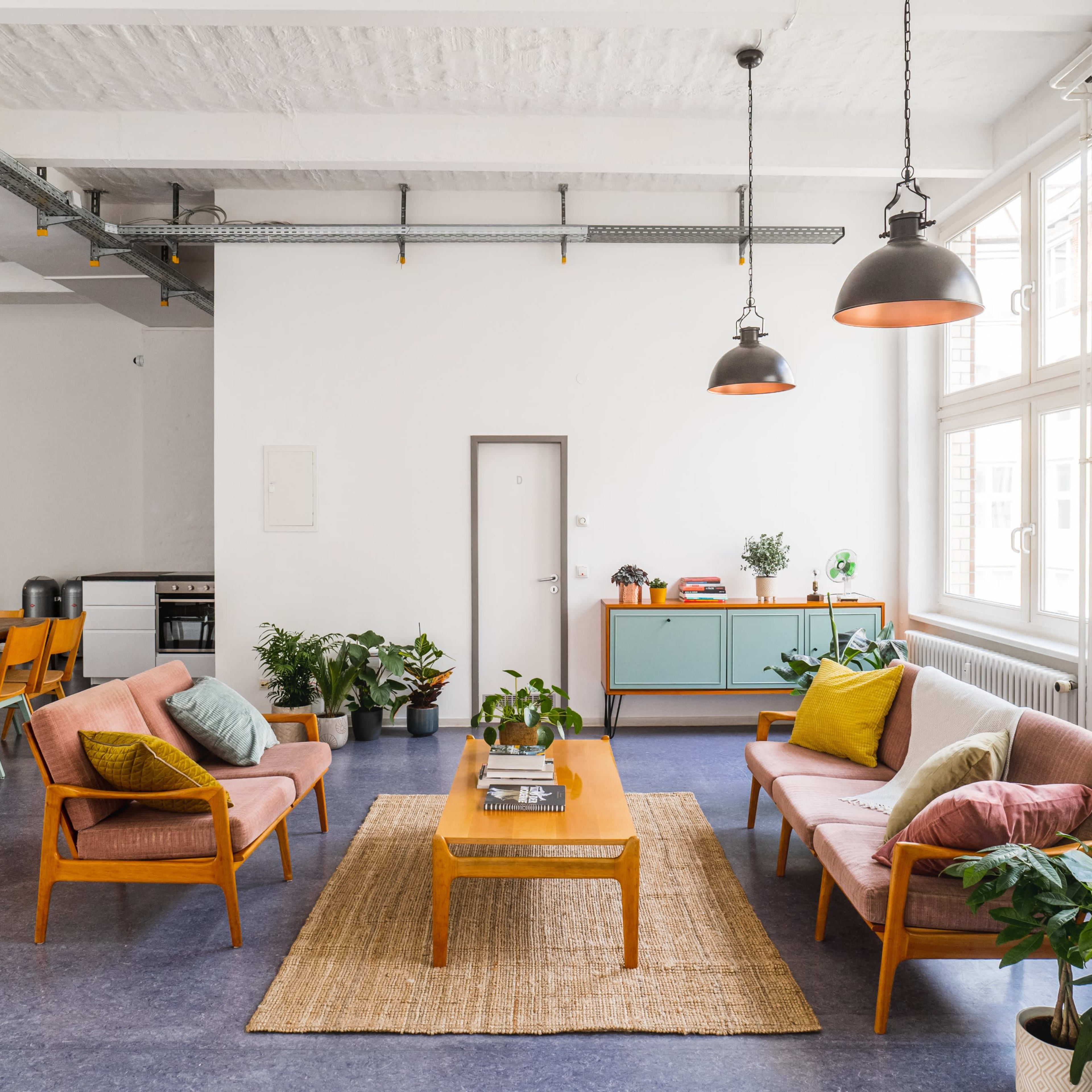 A bright living area with two chairs, a coffee table, and multiple plants, alongside a dining area featuring a wooden table and chairs.