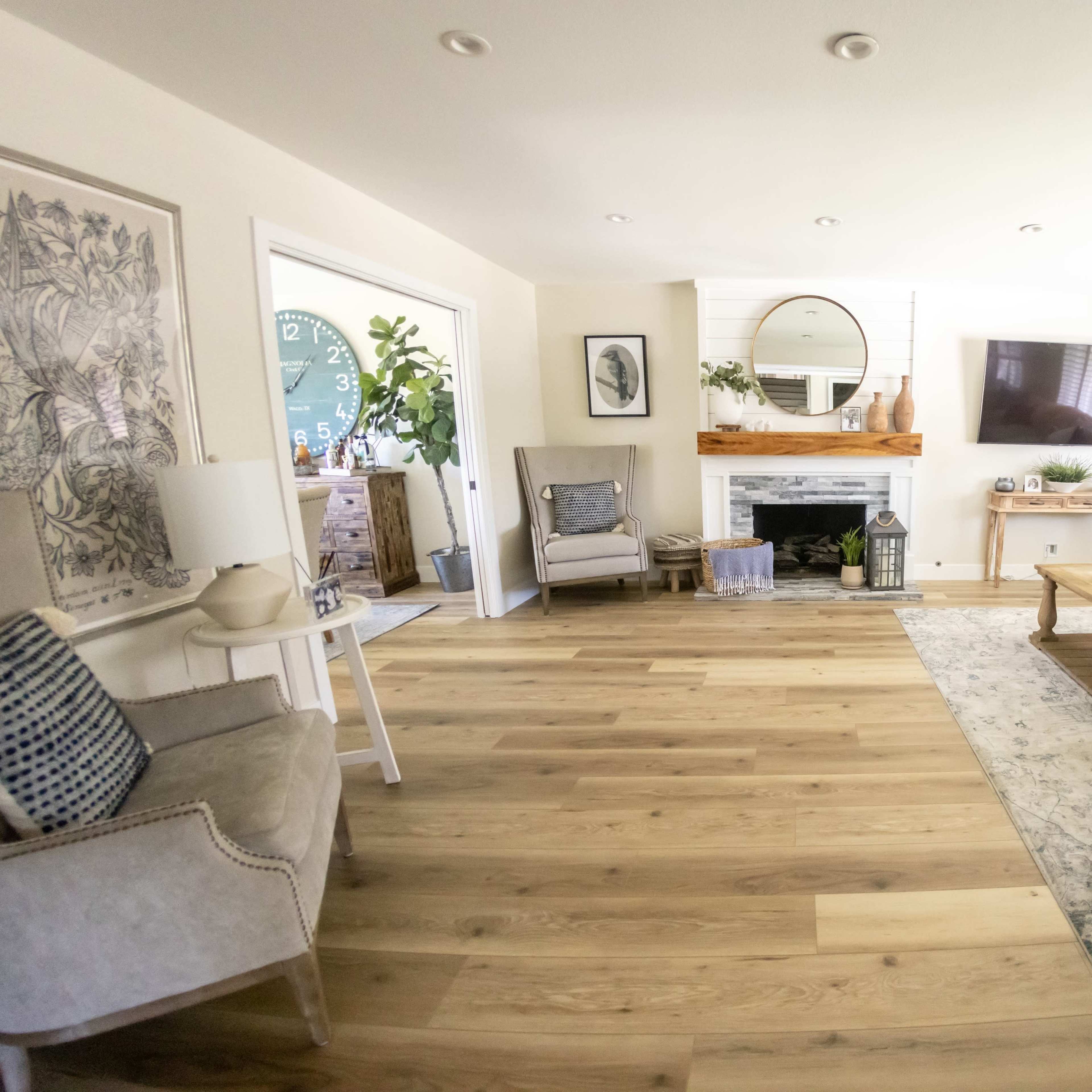 The living room features a light color palette with a fireplace, a large mirror above the mantel, comfortable seating, and hardwood flooring.