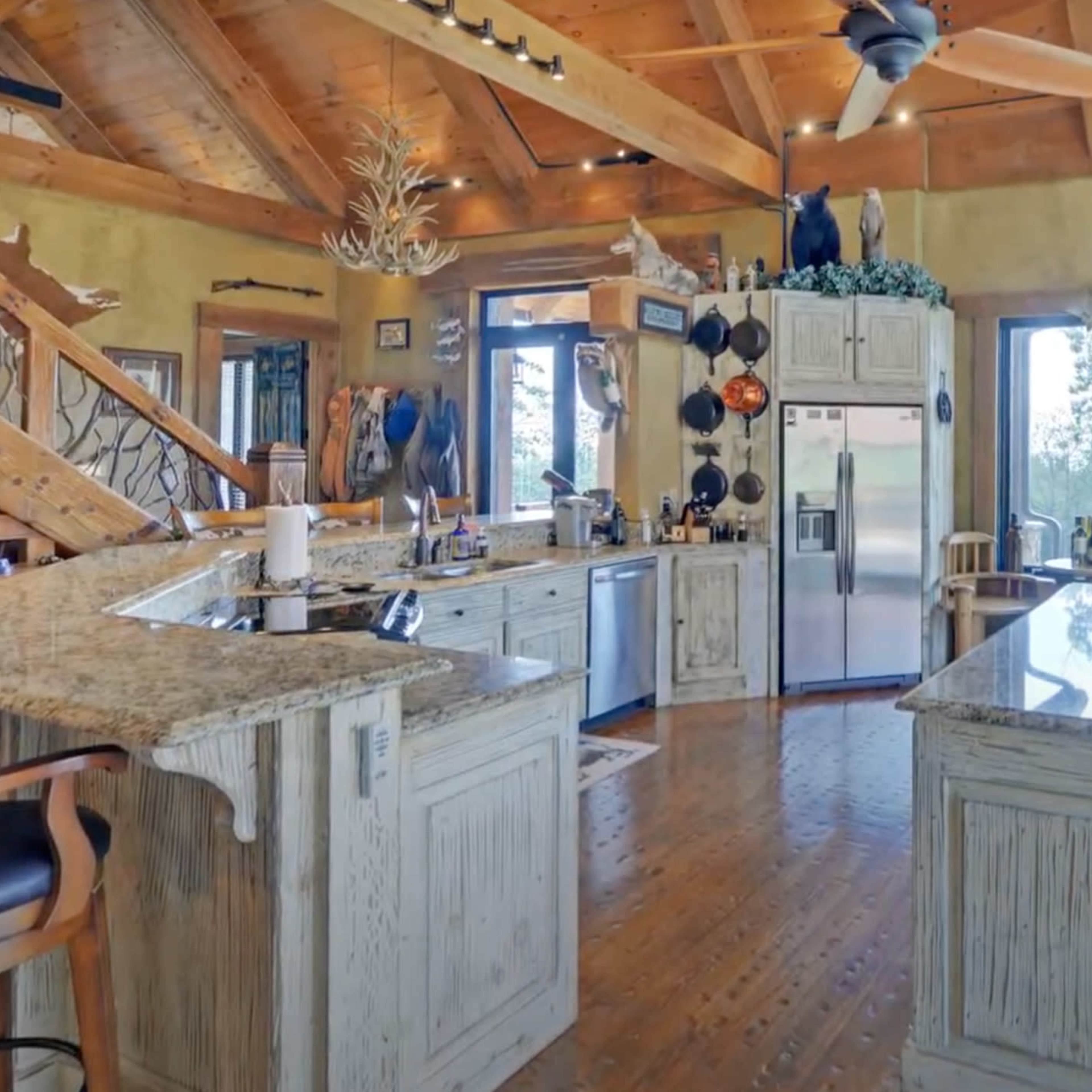 The kitchen features wooden cabinetry, granite countertops, and large windows that offer scenic views.