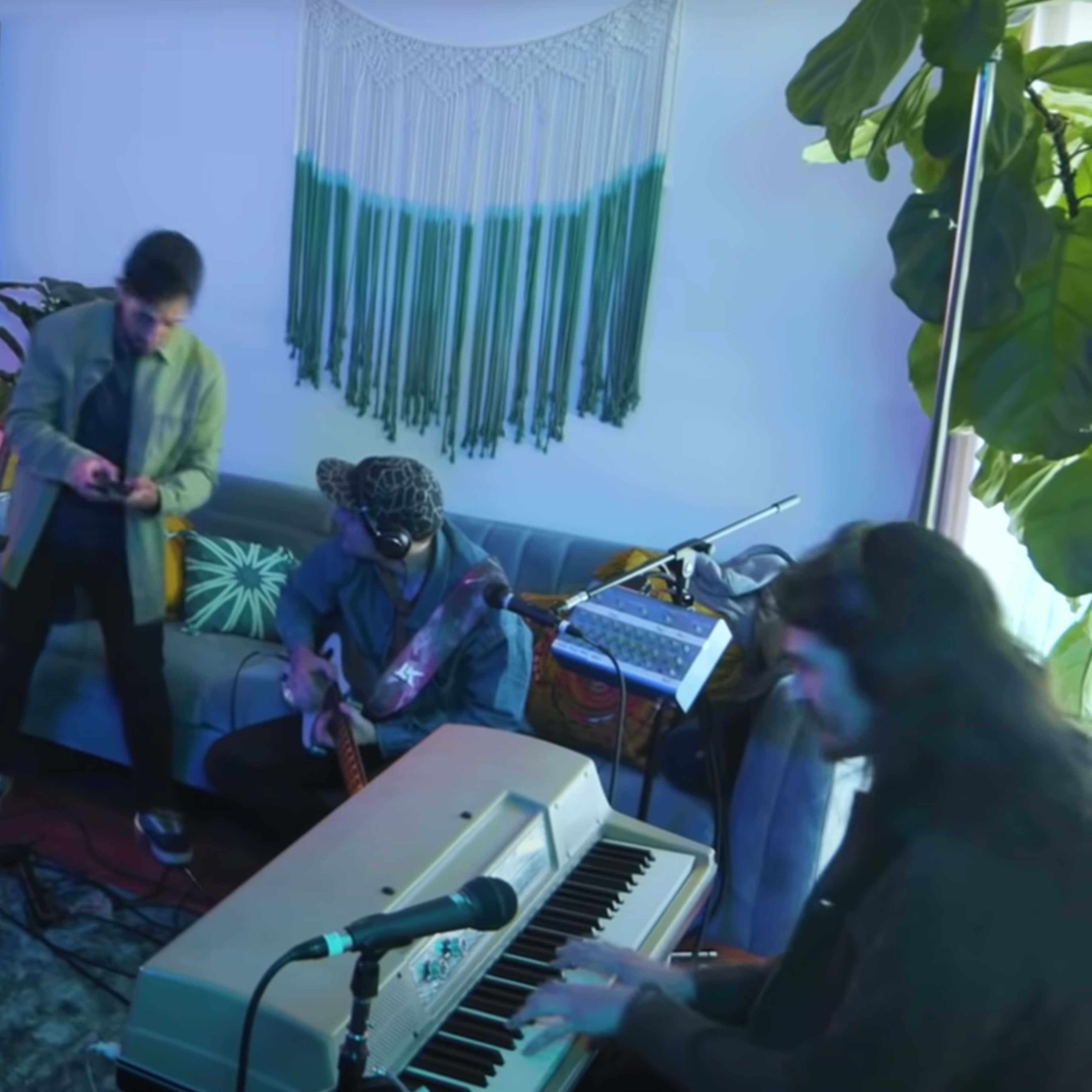 A group of musicians performs in a brightly lit room filled with plants and various instruments.