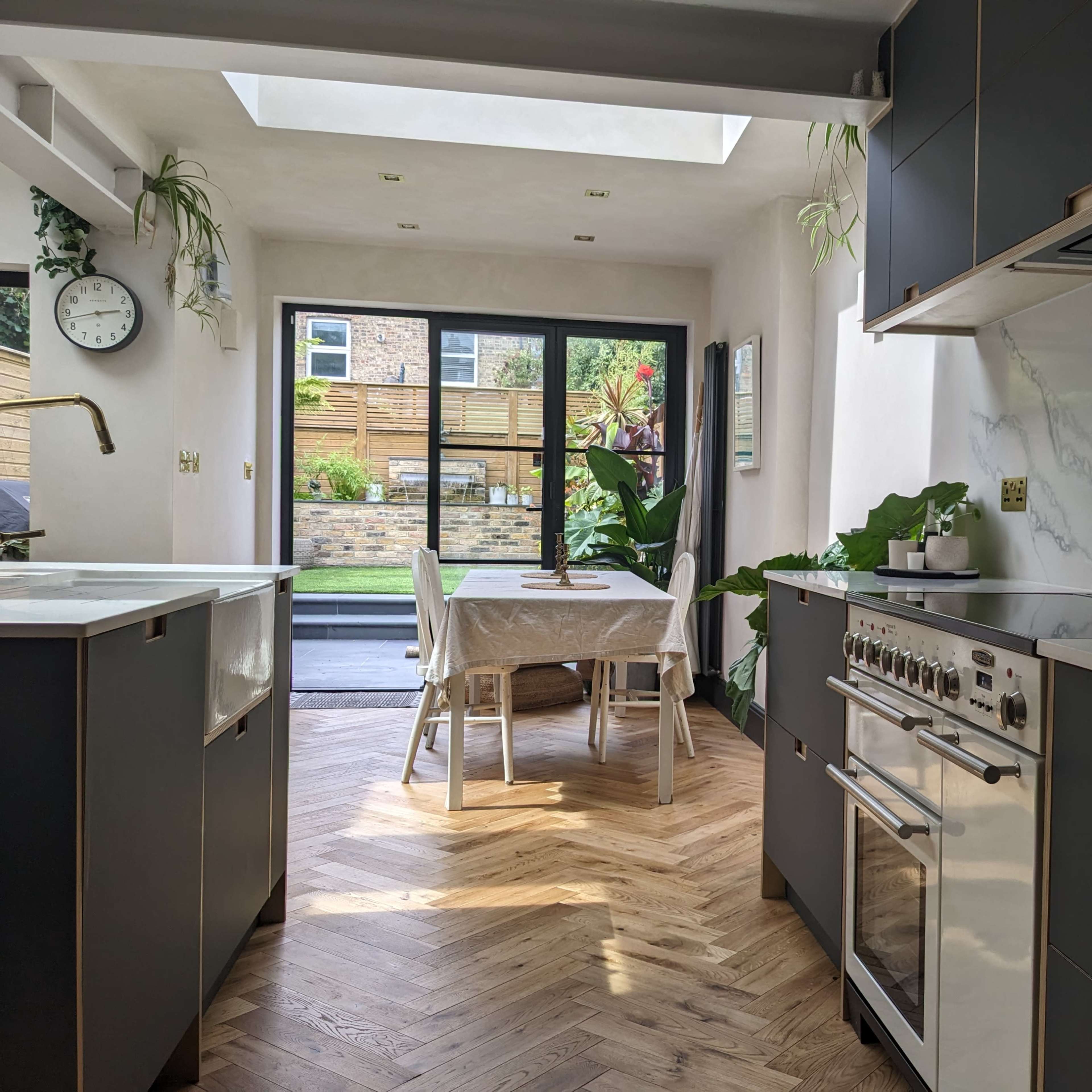A modern kitchen with dark cabinetry, a marble countertop, and a view of a dining area and garden through sliding glass doors.