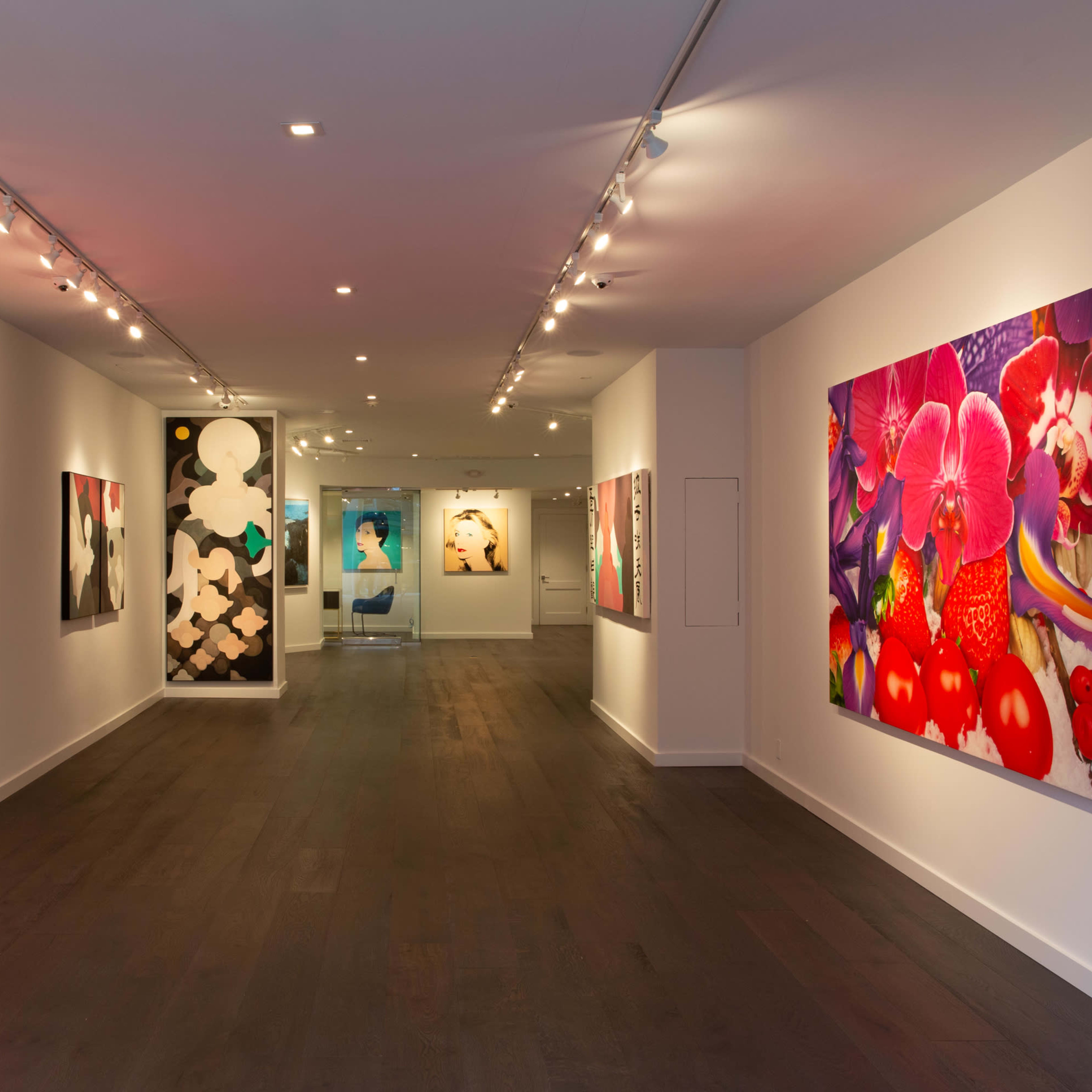 A brightly lit art gallery features large, colorful paintings of flowers and abstract designs on the walls.