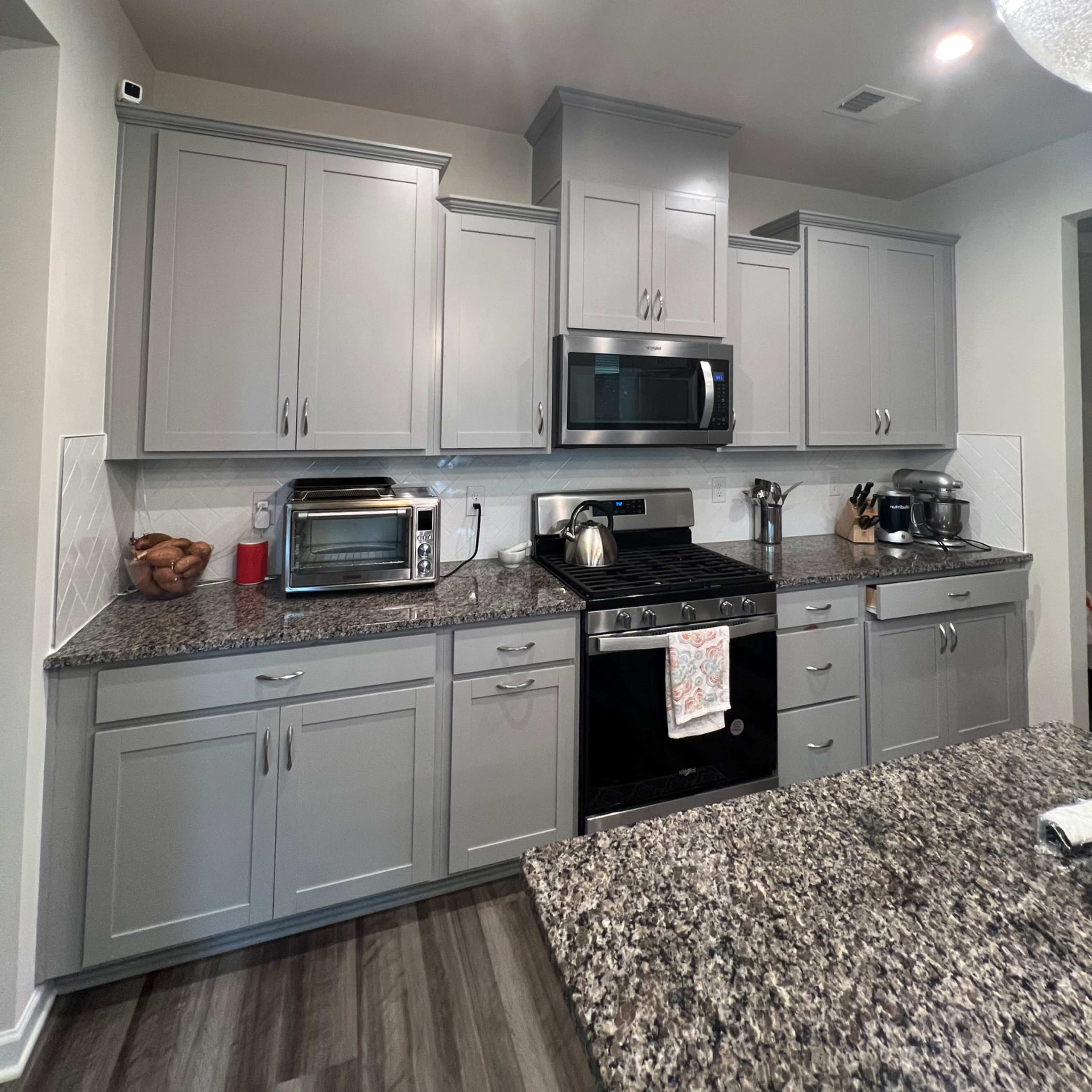 A modern kitchen with gray cabinets, a black oven, stainless steel appliances, and a granite countertop.