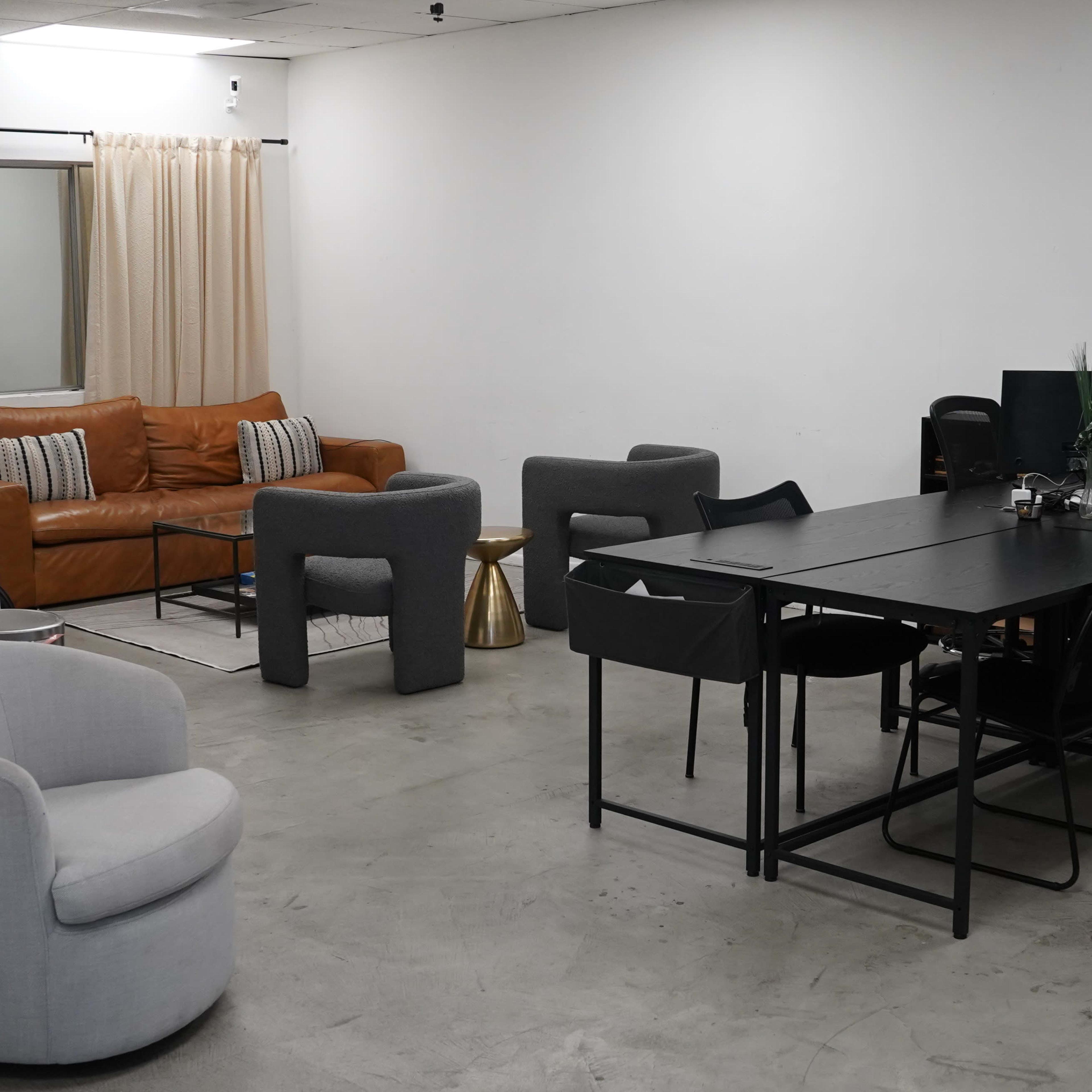 A minimalist office space featuring a brown leather couch in a seating area and a large black table surrounded by various chairs.