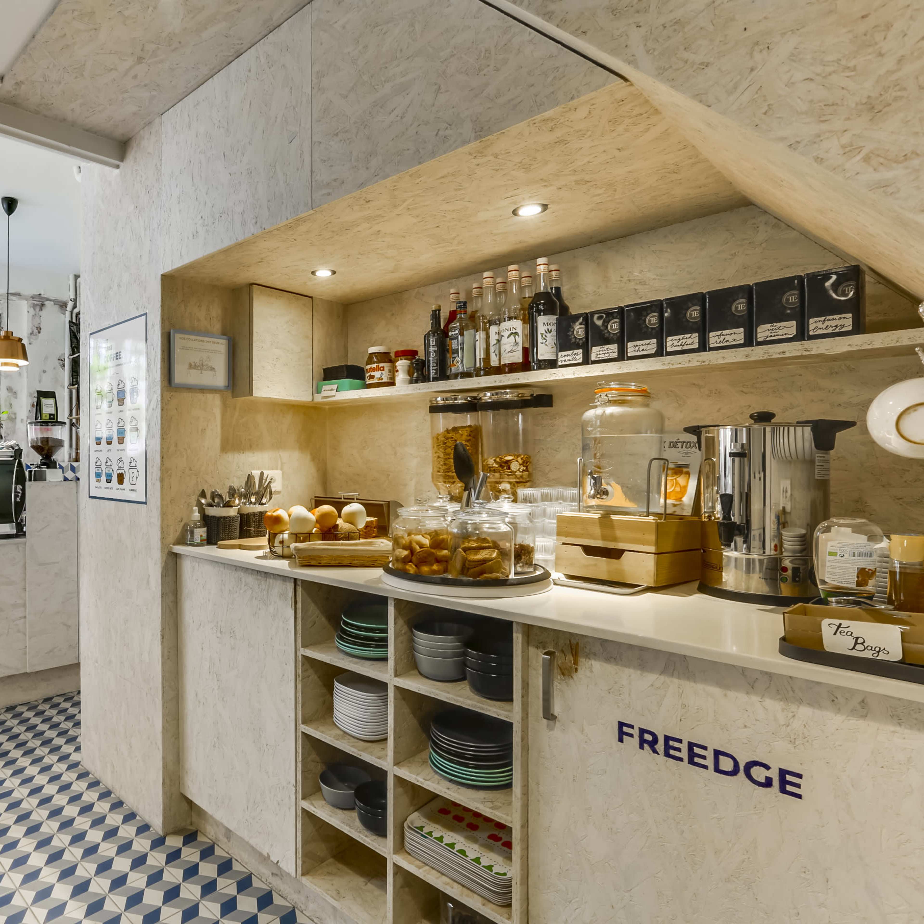 A modern café interior featuring a service counter with glass jars of food, shelves for drinks, and a coffee machine in an inviting space with patterned tile flooring.