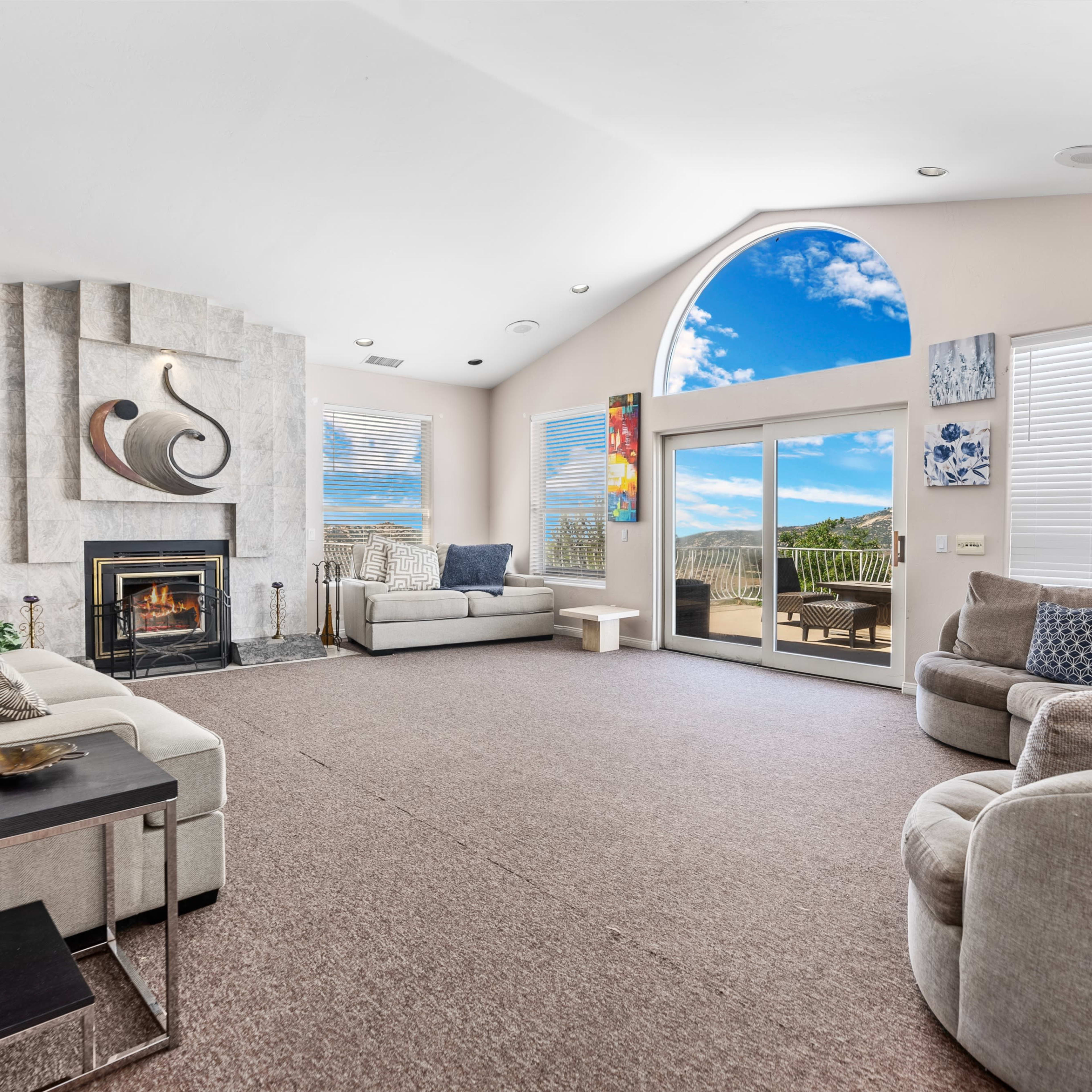 The living room features two light-colored sofas, a stone fireplace, and large windows with a view of the outdoors.