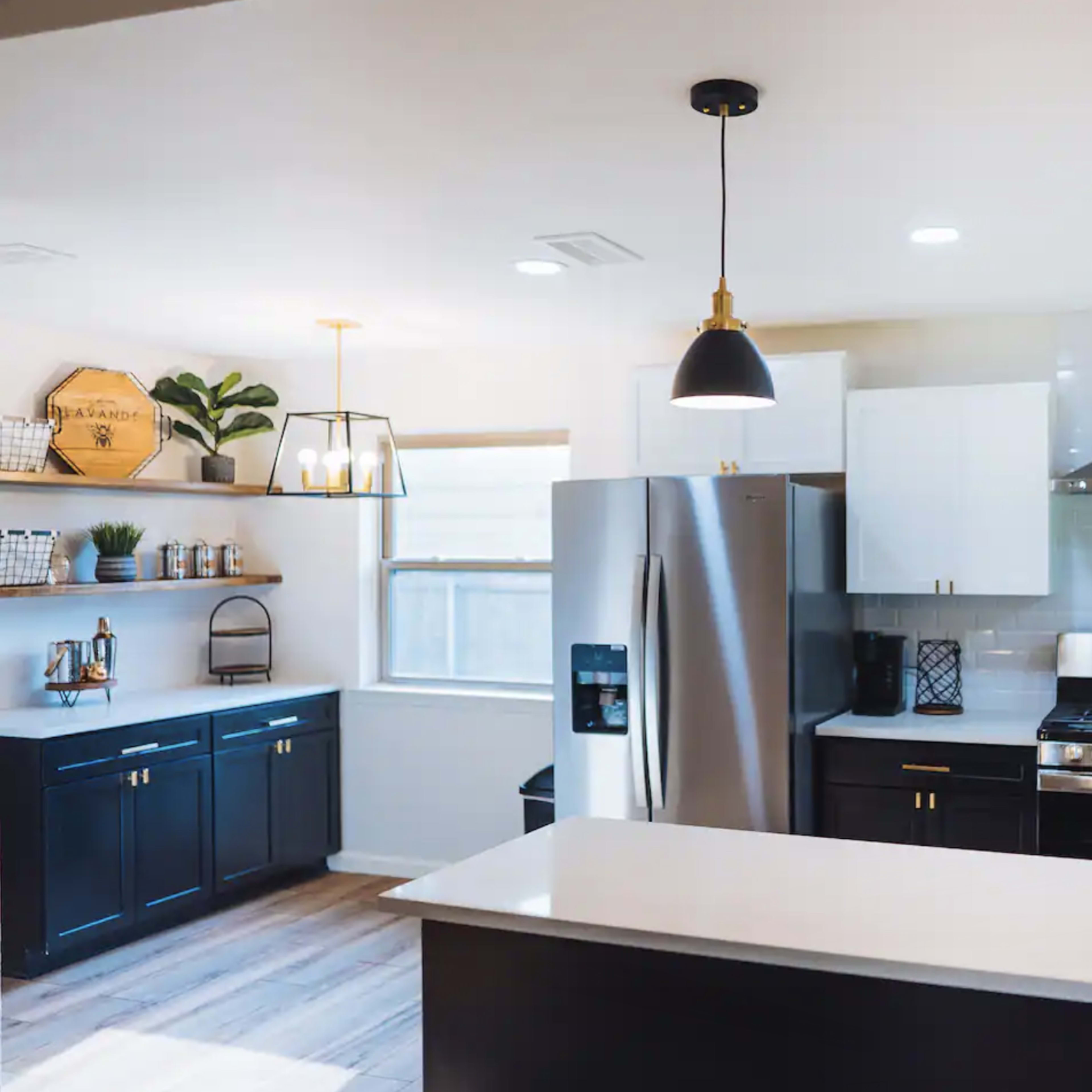A modern kitchen with stainless steel appliances, white upper cabinets, black lower cabinets, and pendant lighting.