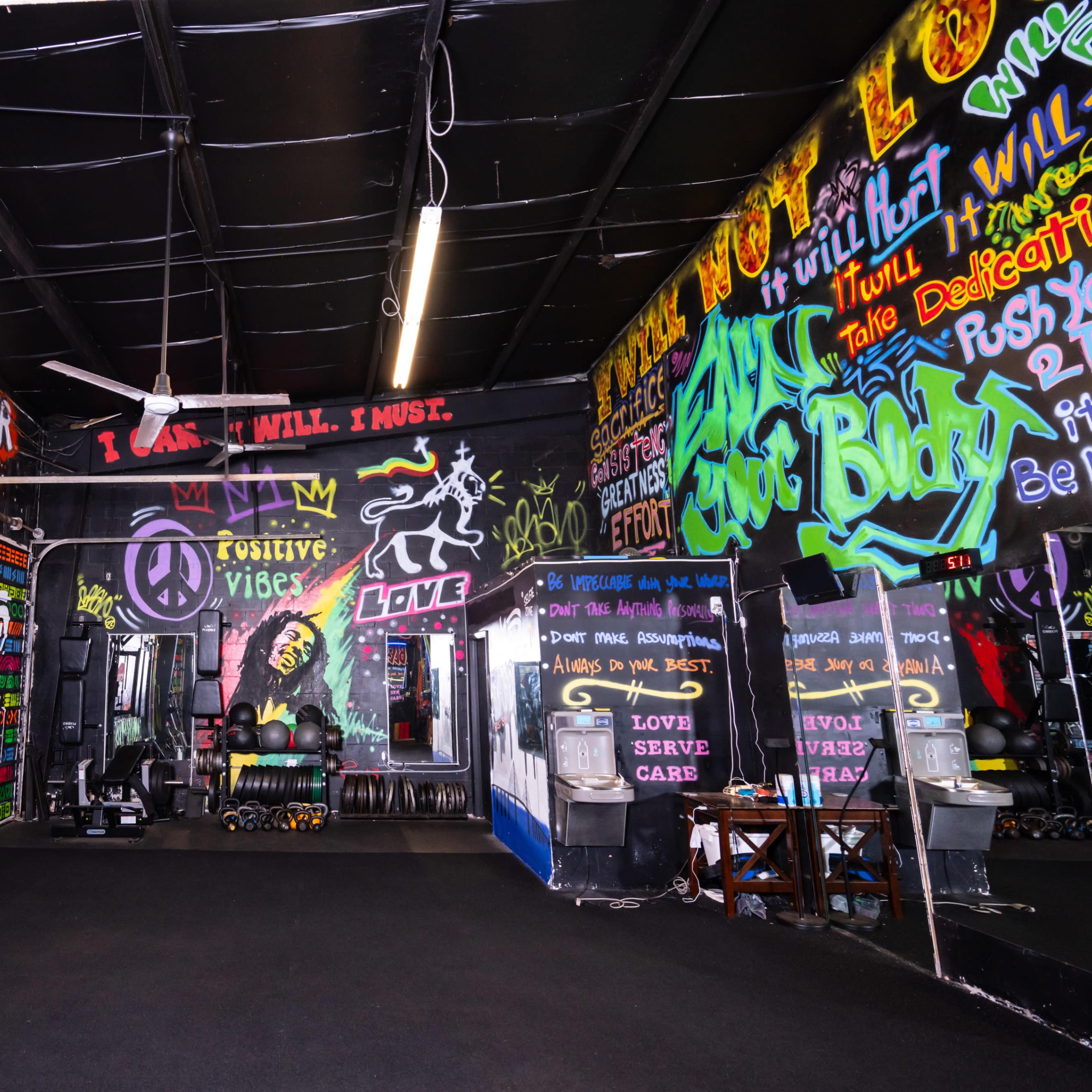A vibrant gym interior adorned with colorful graffiti and motivational phrases on the walls.