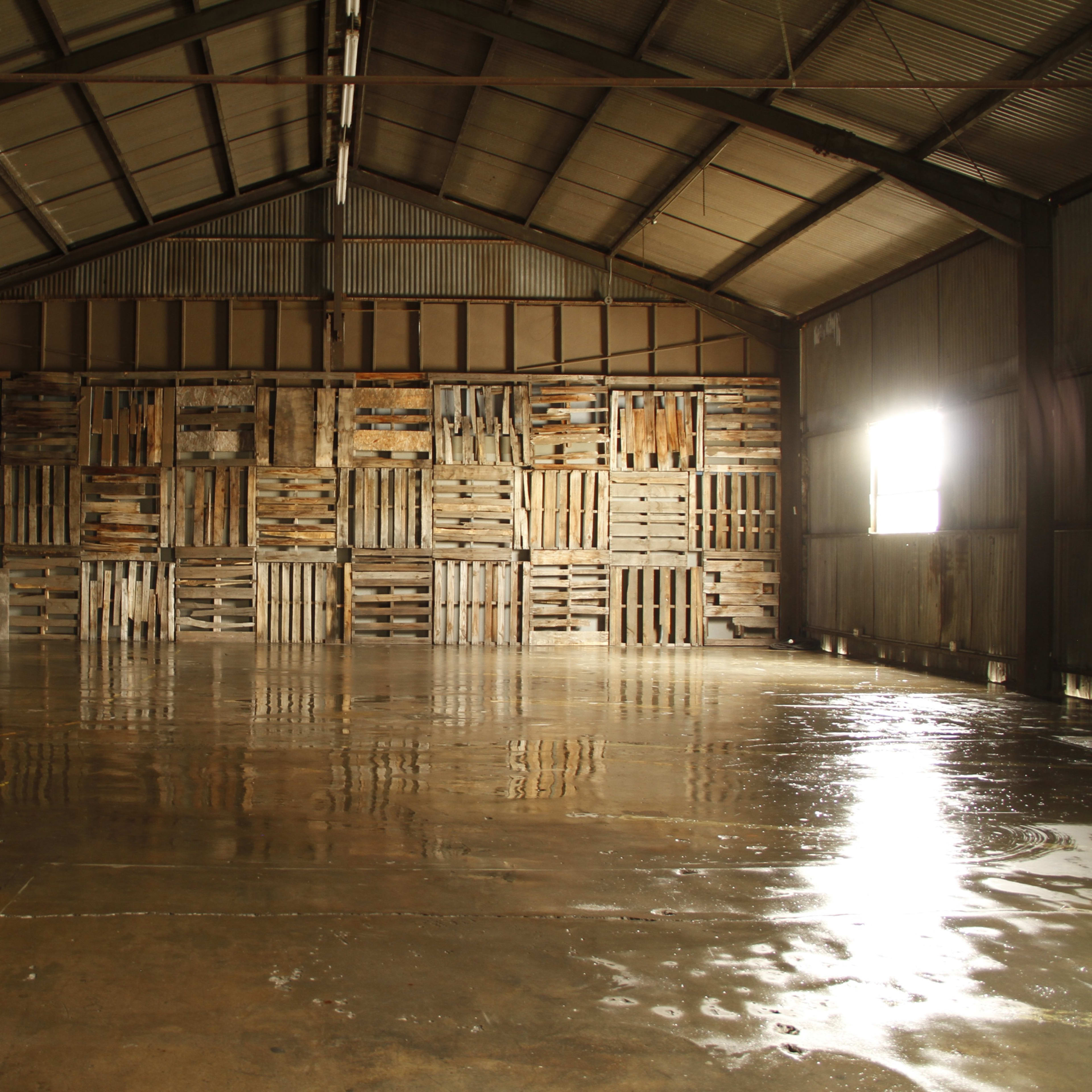 An empty warehouse interior with a polished concrete floor and wooden pallets stacked against one wall.