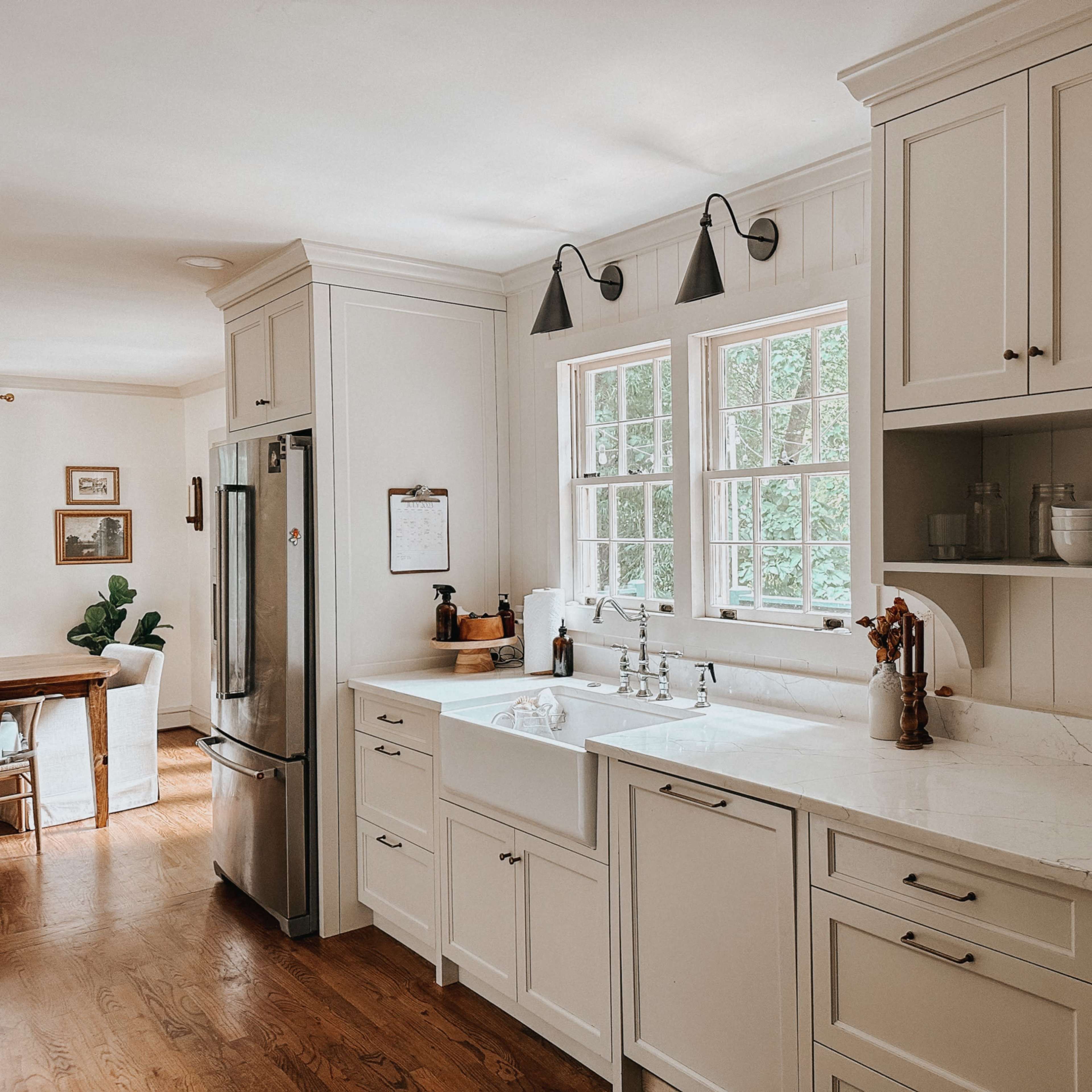 A modern kitchen with white cabinetry, a farmhouse sink, and a large window overlooking greenery.