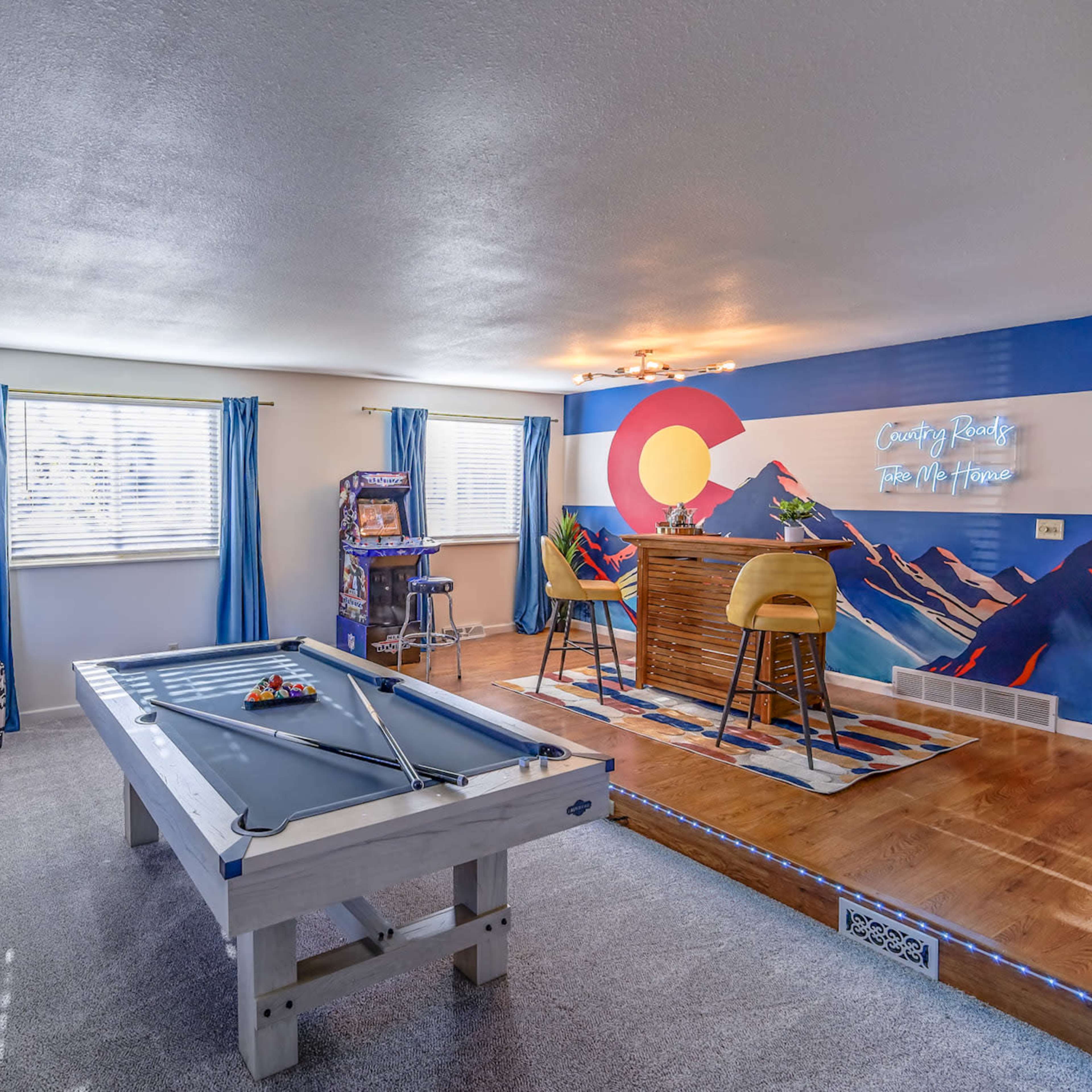A game room featuring a pool table, a bar area with stools, and a cozy seating nook.