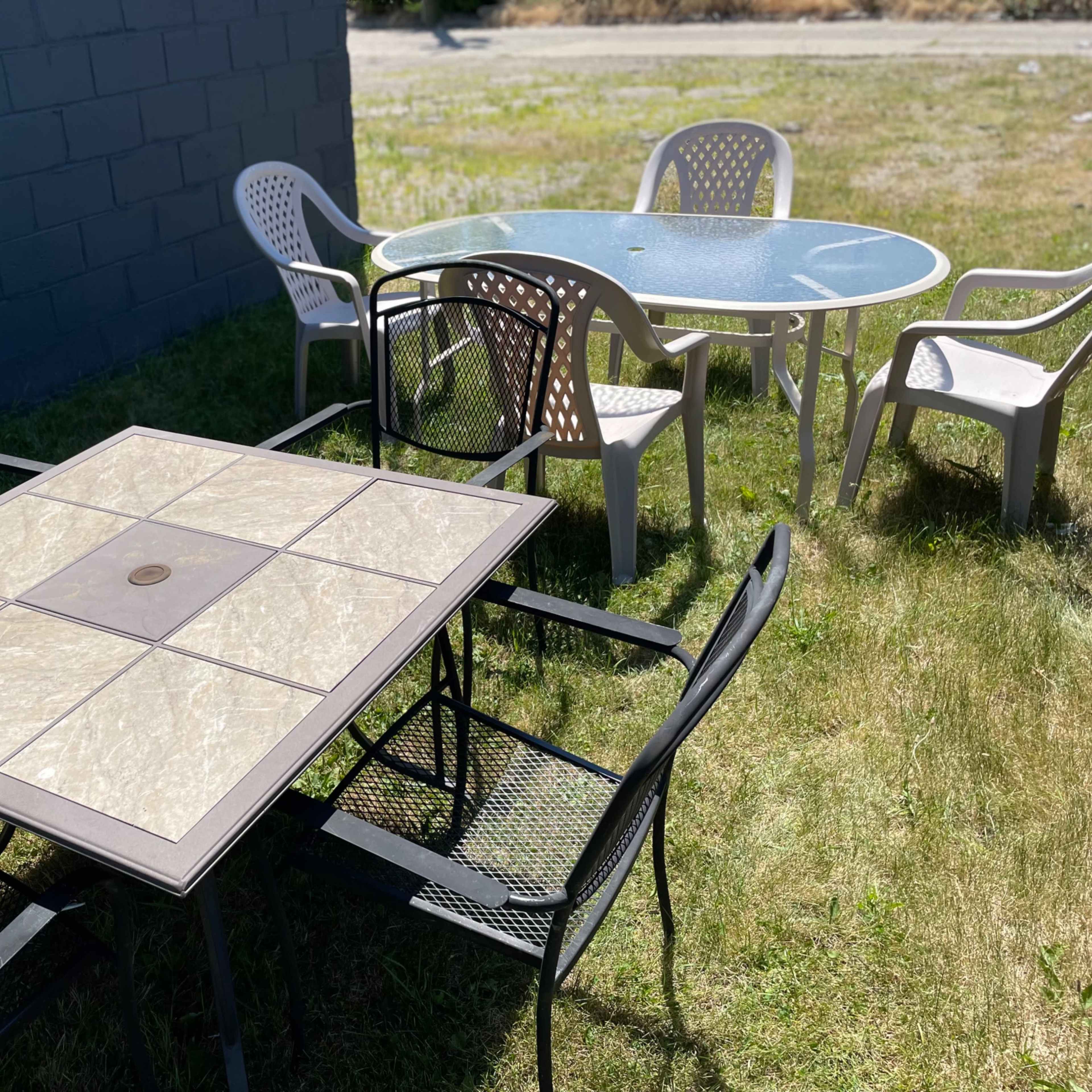 A set of outdoor tables and chairs sits on a grassy area beside a gray wall.