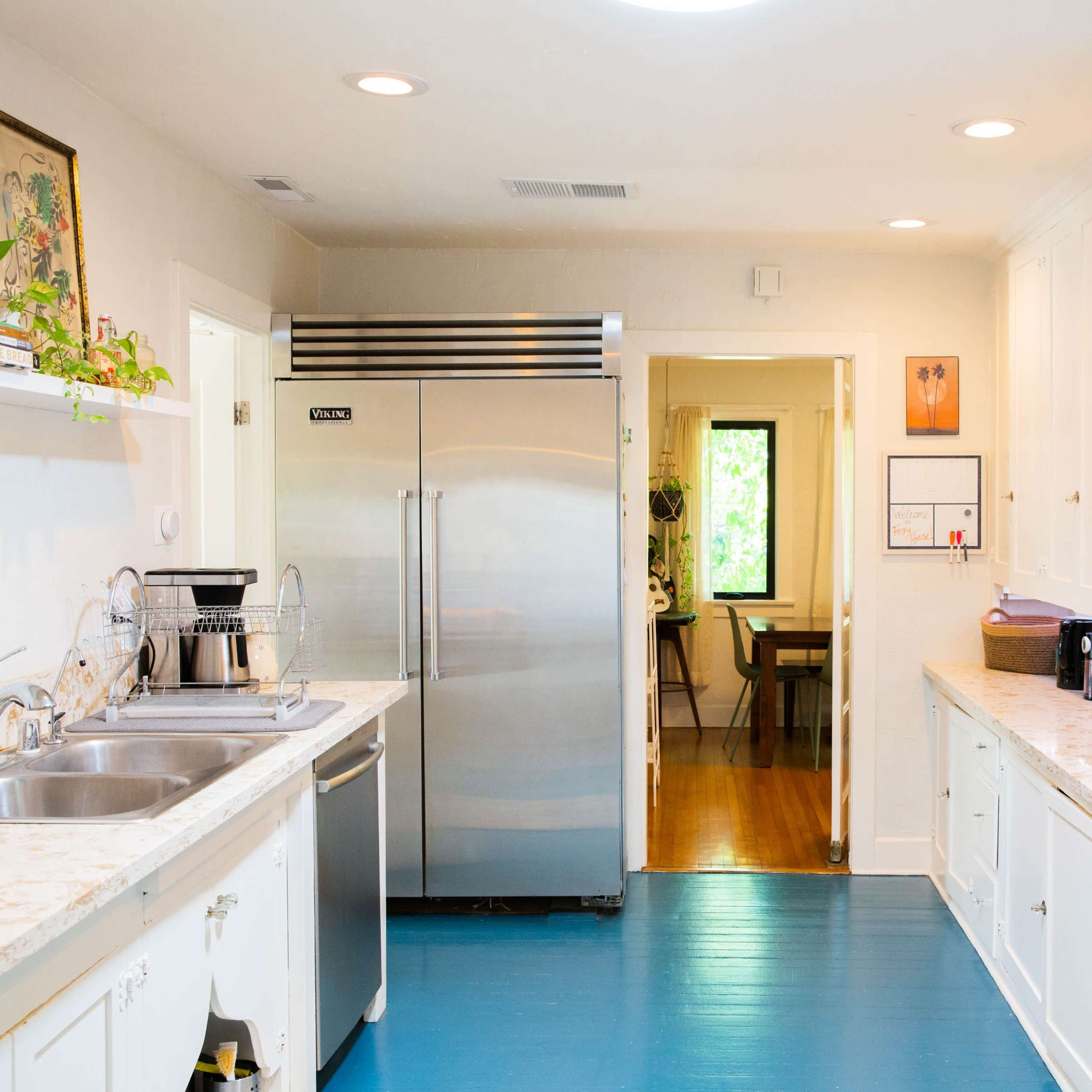 A modern kitchen features white cabinetry, stainless steel appliances, and a blue floor, with a doorway leading to another room in the background.