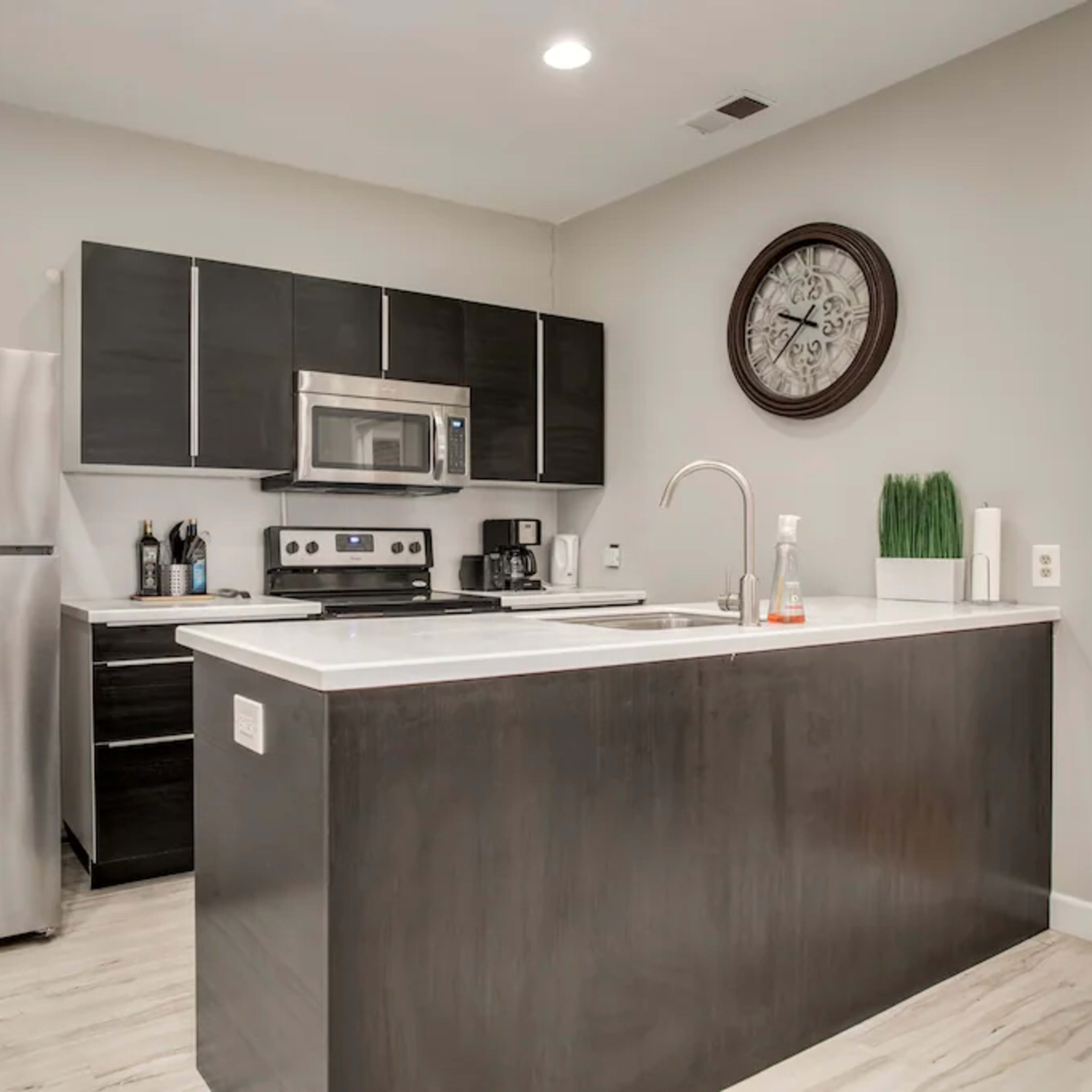 A modern kitchen with dark cabinetry, stainless steel appliances, and a central island with a sink.