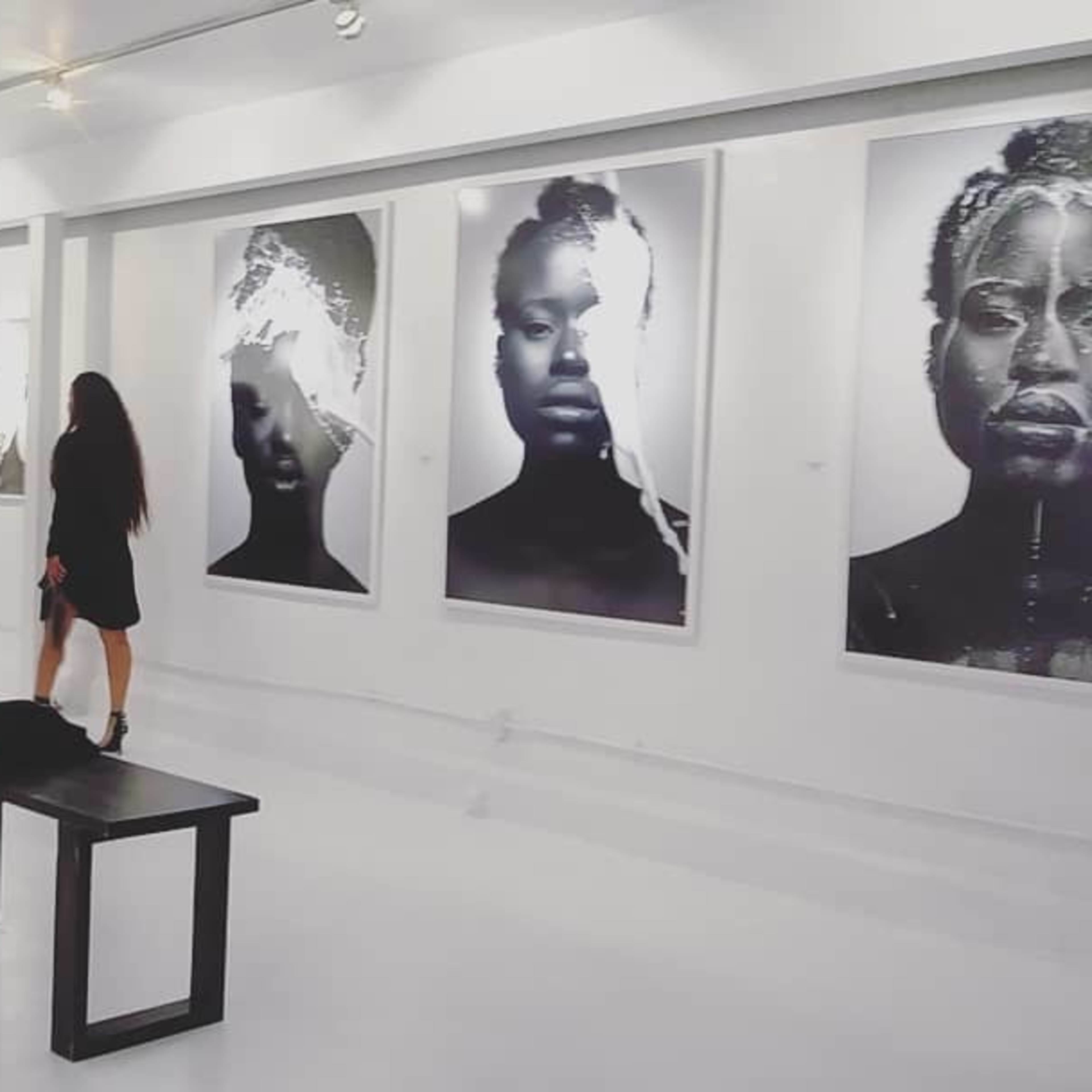 People interacting in an art gallery with large black and white photographs of faces displayed on white walls.