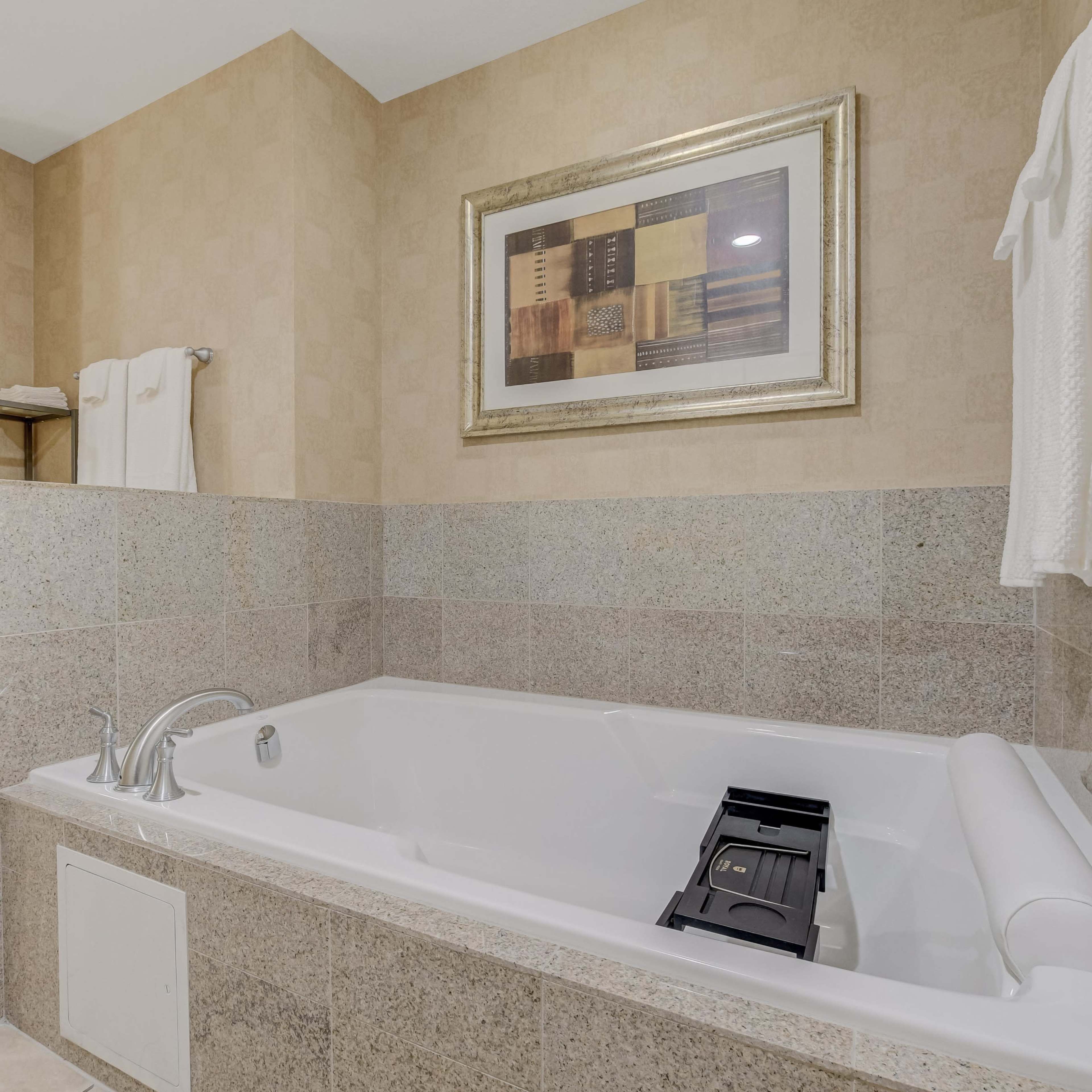 A modern bathroom features a jetted bathtub, a glass-enclosed shower, and beige stone walls.