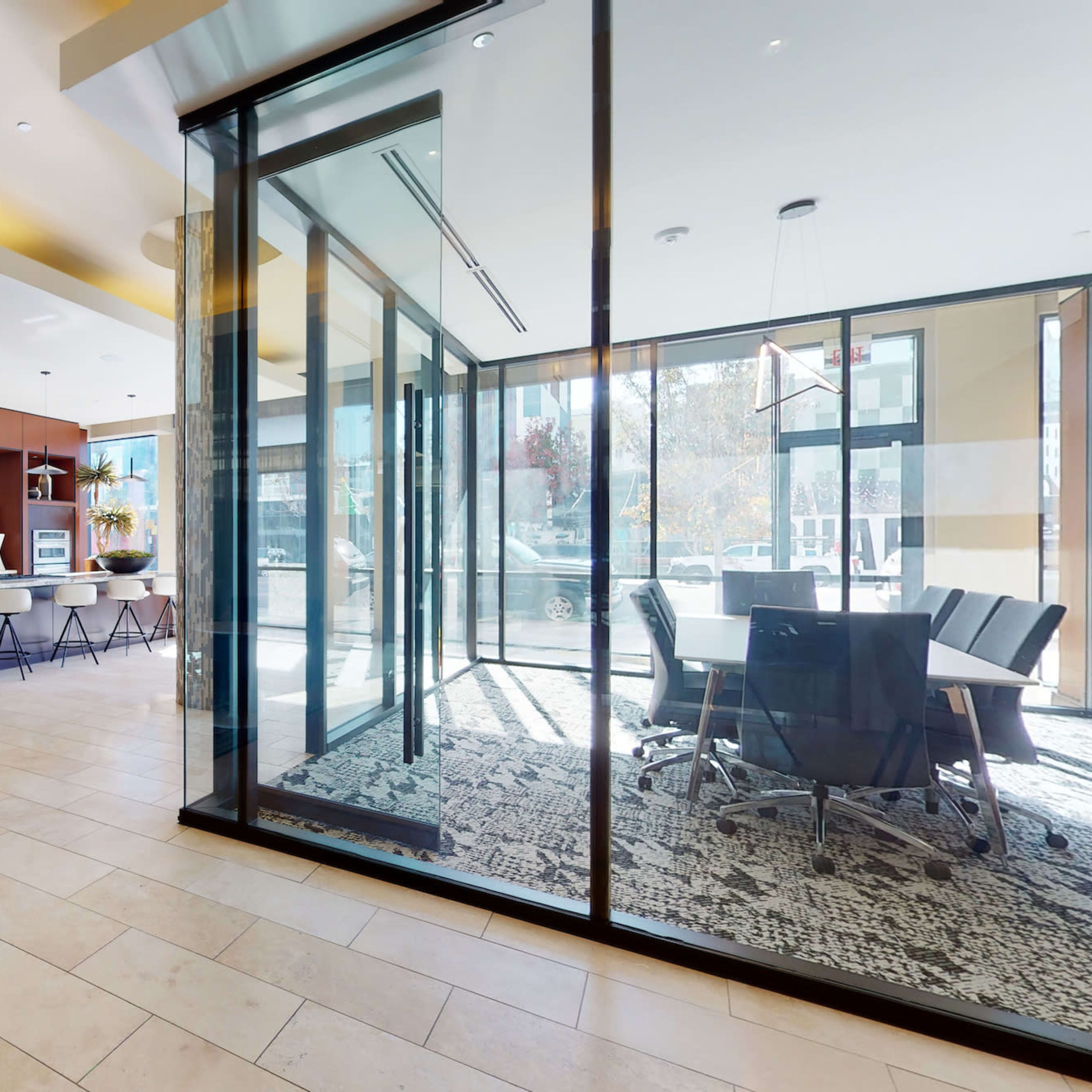 A modern lounge area with a seating arrangement, a kitchenette, and a glass-walled conference room.