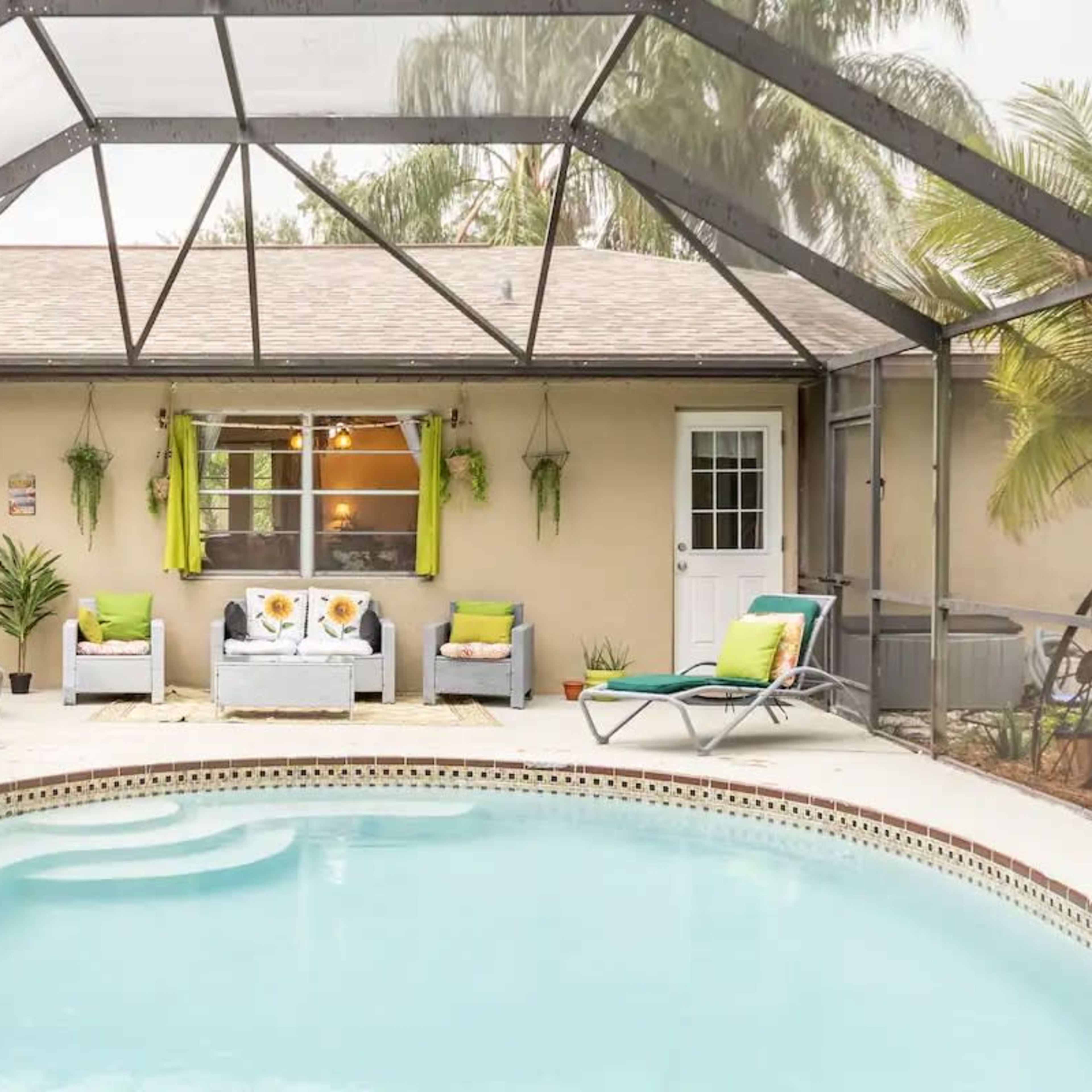 A screened patio features a swimming pool surrounded by lounge chairs and a seating area with vibrant cushions.