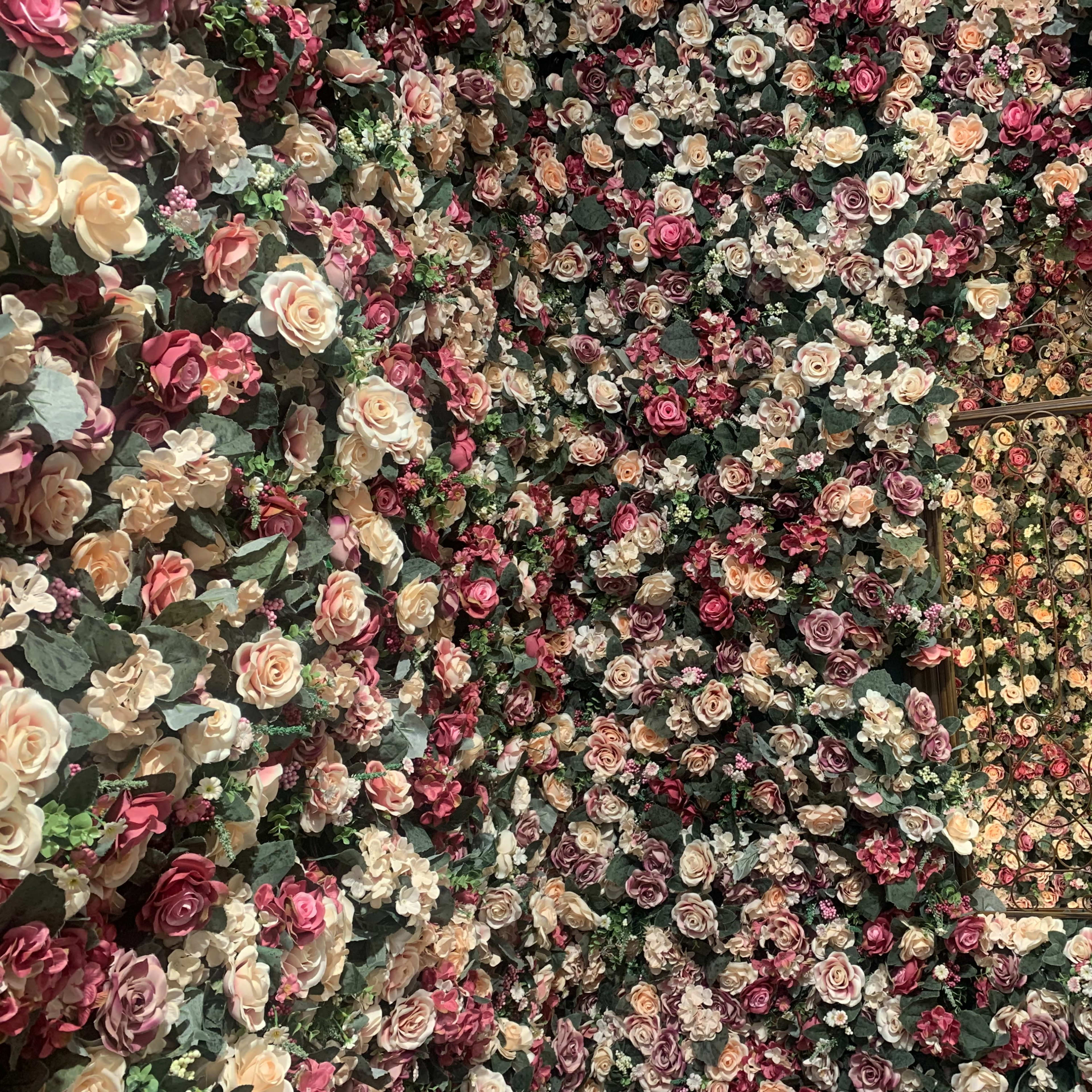 A room with walls covered in artificial roses in various colors, along with a decorative iron grill window.
