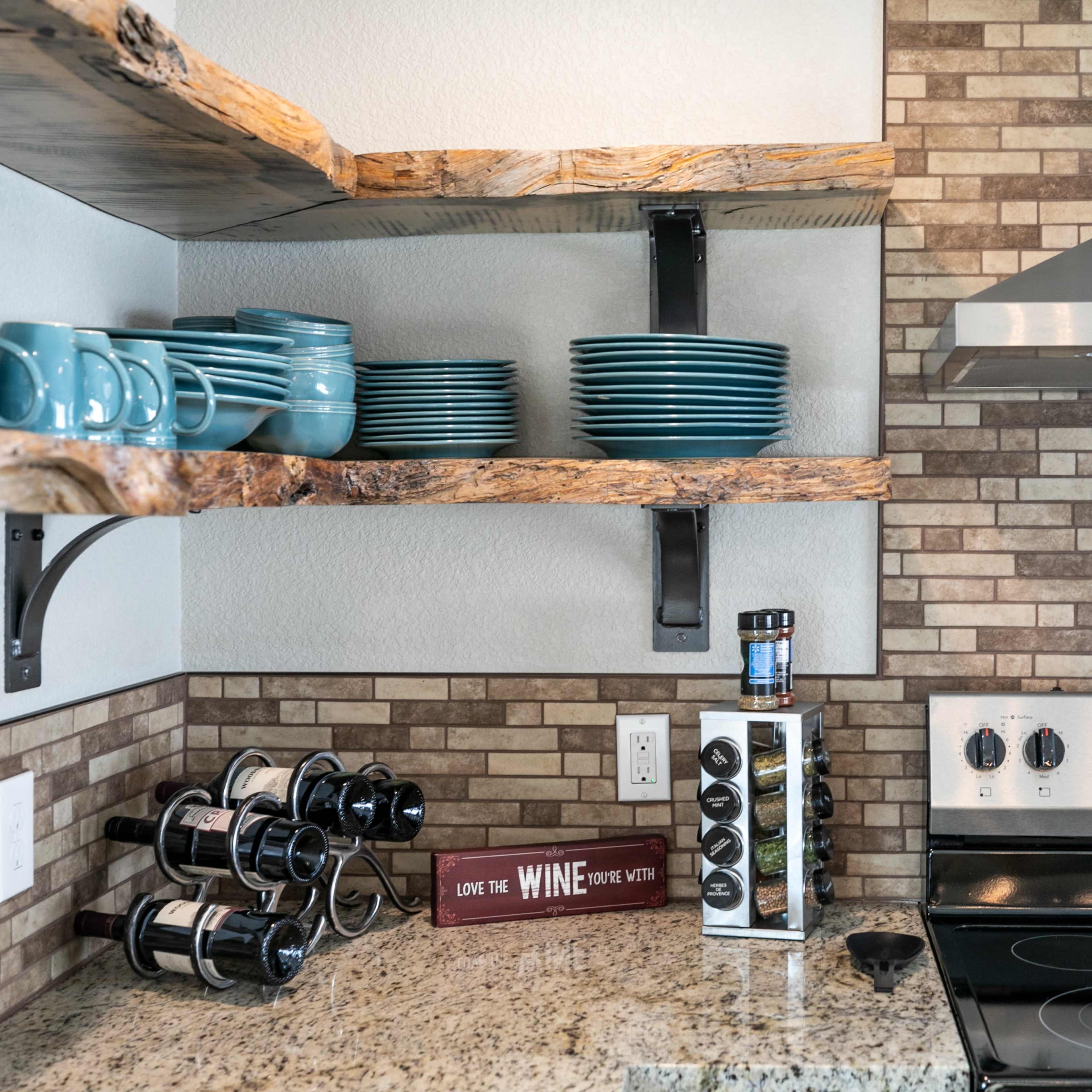 A modern kitchen with wooden shelves holding blue dishes, a stainless steel stove, and a wine rack against a tiled wall.