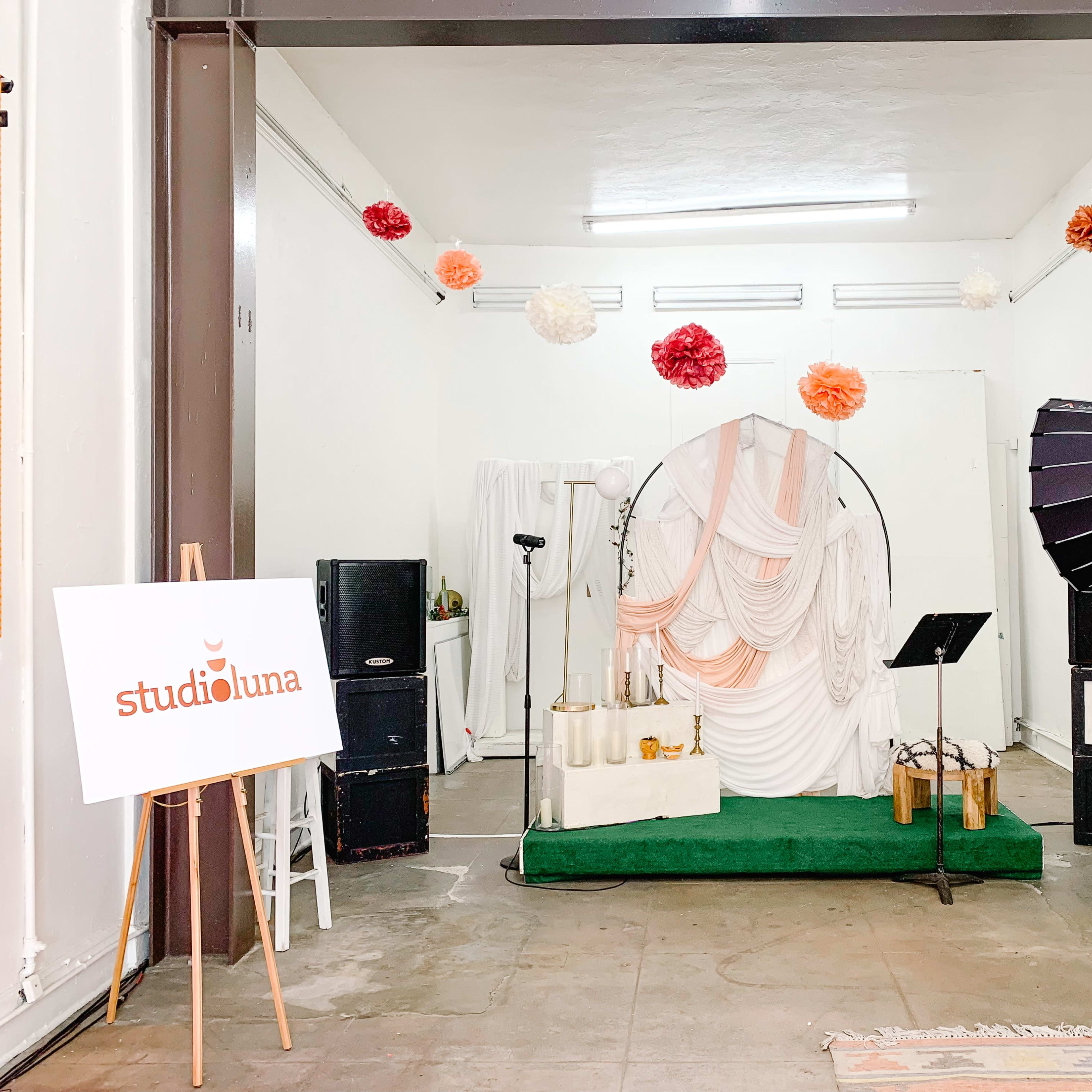 A decorated studio space with a white backdrop, a circular frame, draped fabric, two speakers, and a sign for "studioluna."
