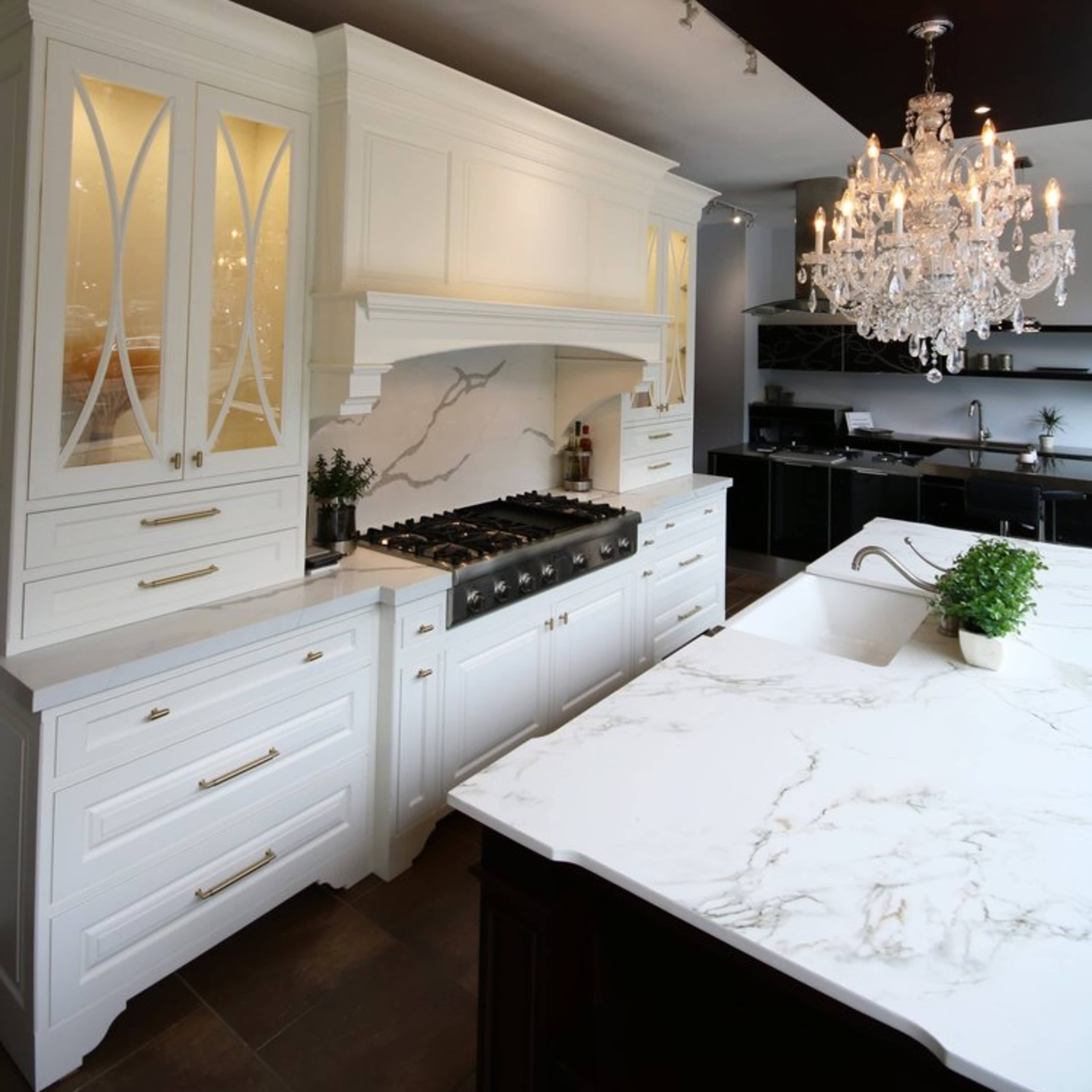 A modern kitchen features white cabinetry, a marble countertop, and a large chandelier overhead.