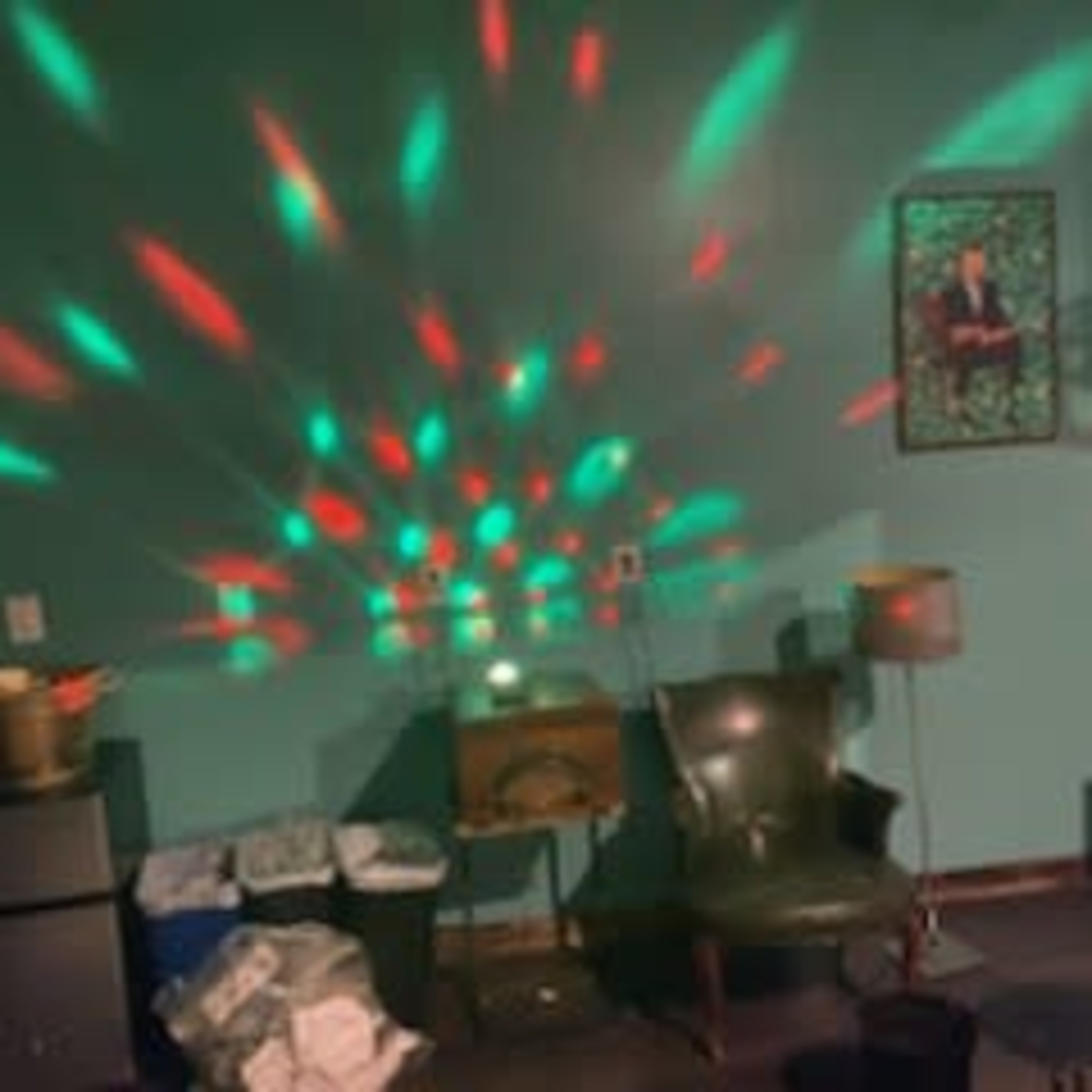 A room with a green wall, featuring chairs, a table, decorative lighting patterns on the wall, and a framed picture.