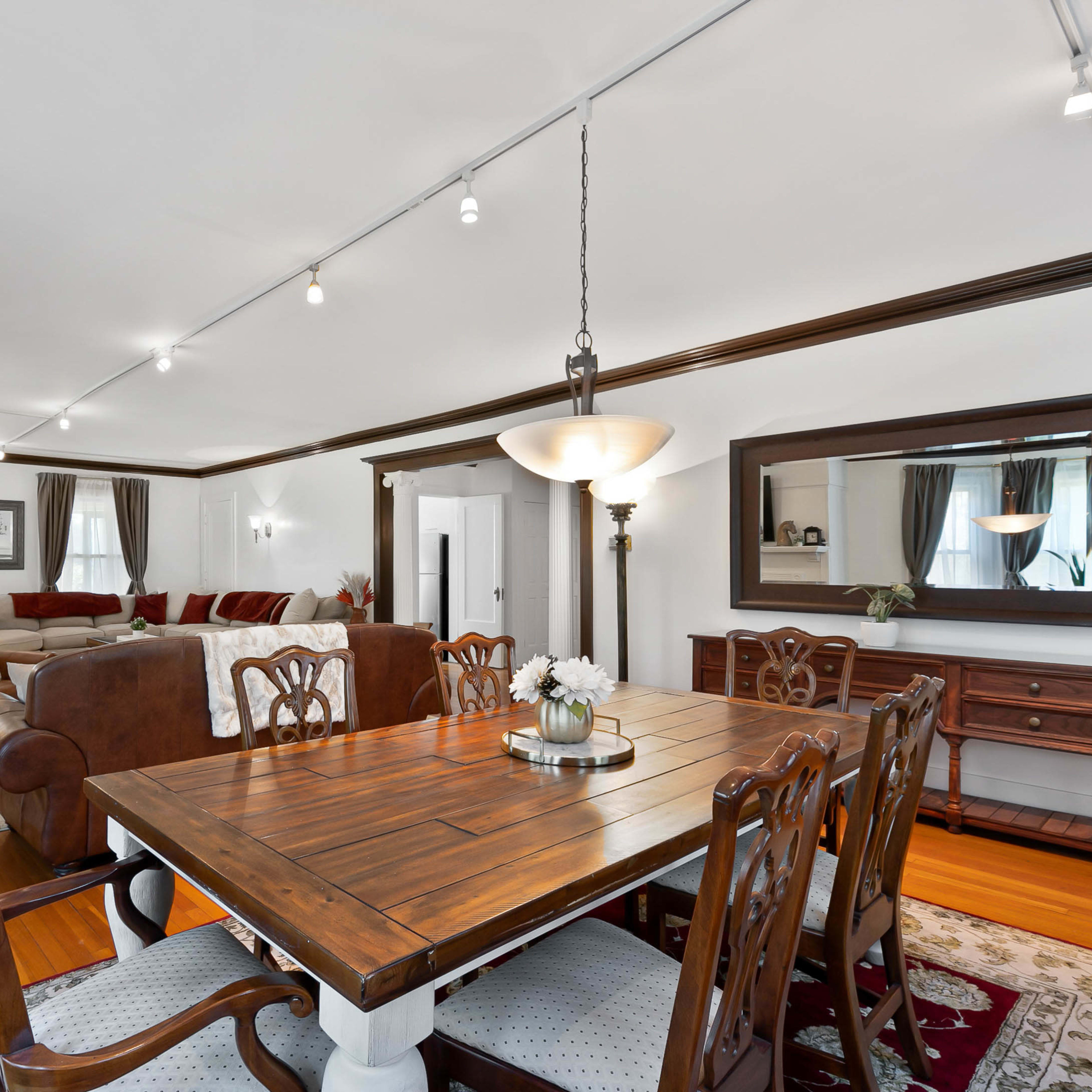 A spacious living and dining area features a wooden dining table surrounded by upholstered chairs, with a sectional sofa and a fireplace in the background.