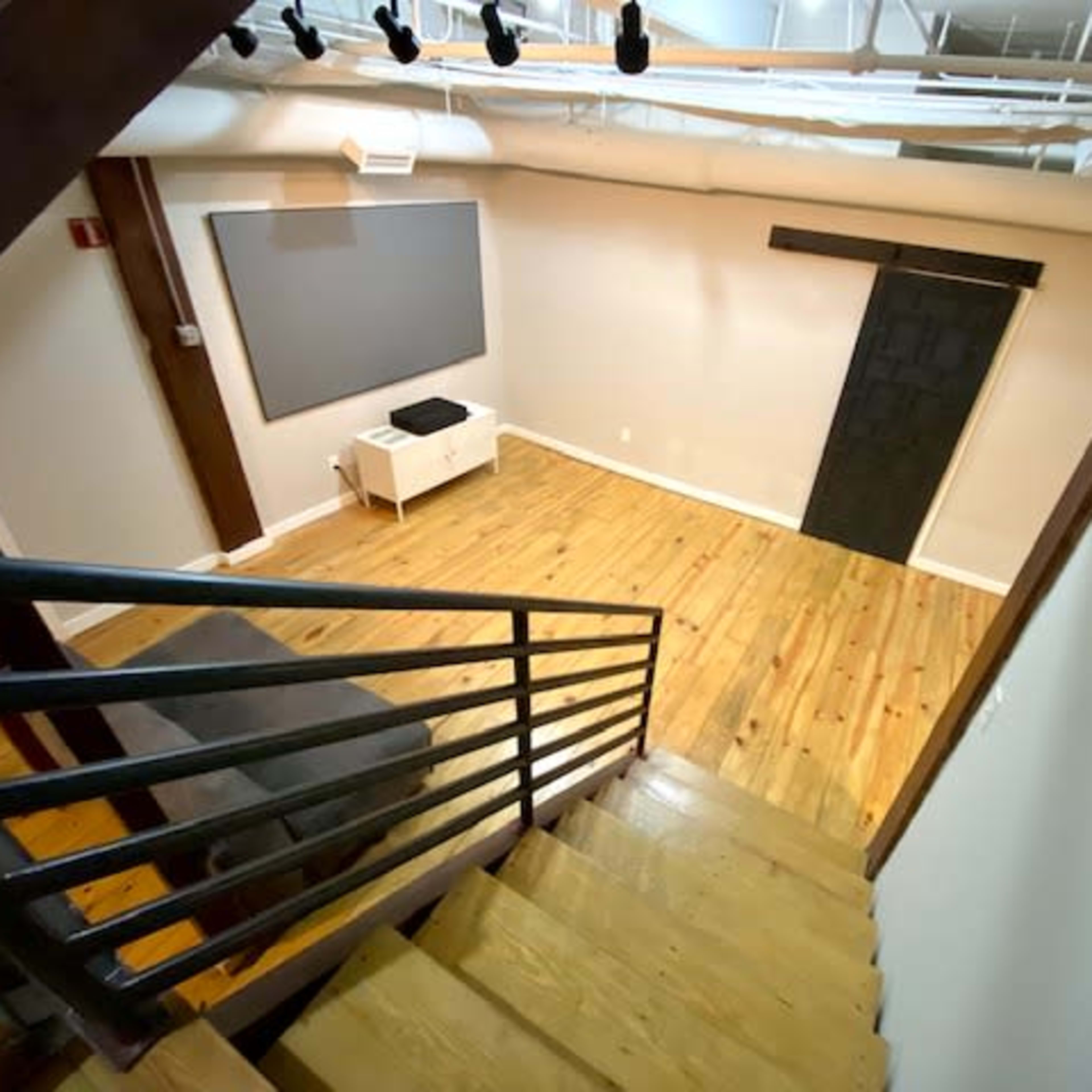 A staircase leads down to a room with wooden floors, a gray wall, and a black sliding door.