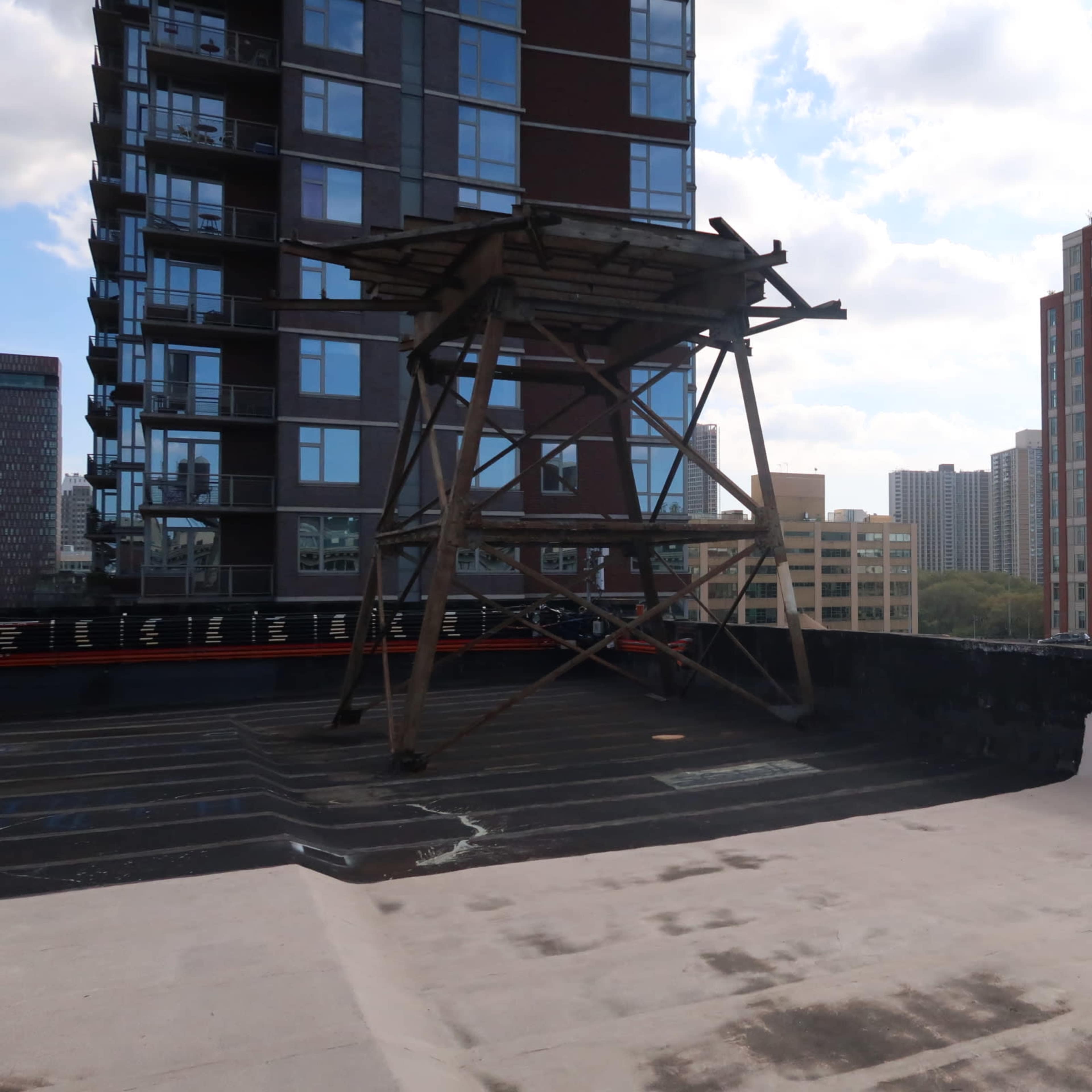 A concrete rooftop features a wooden frame structure and overlooks nearby high-rise buildings against a cloudy sky.