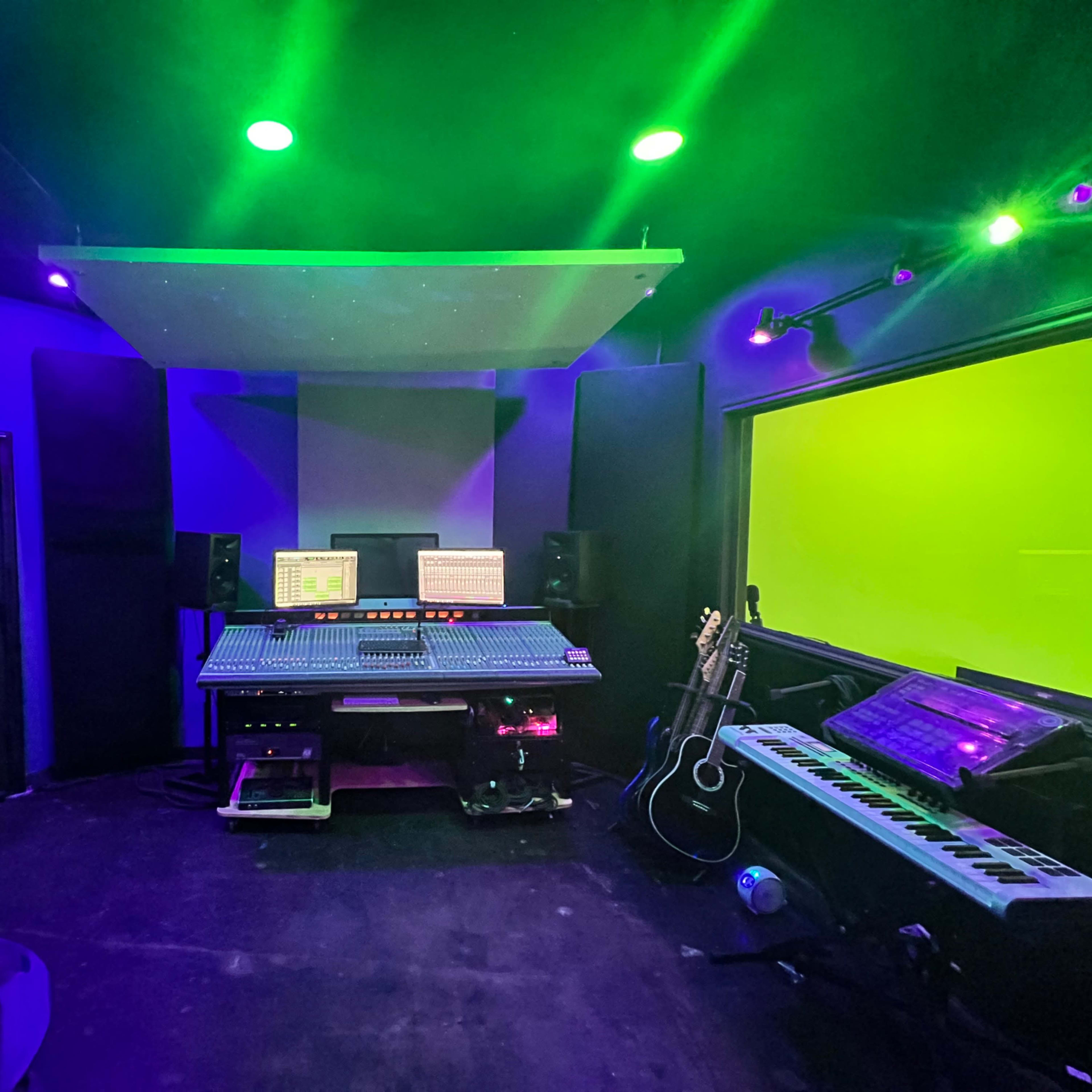 A music recording studio featuring a large mixing console, speakers, and various musical instruments, with purple and green ambient lighting.