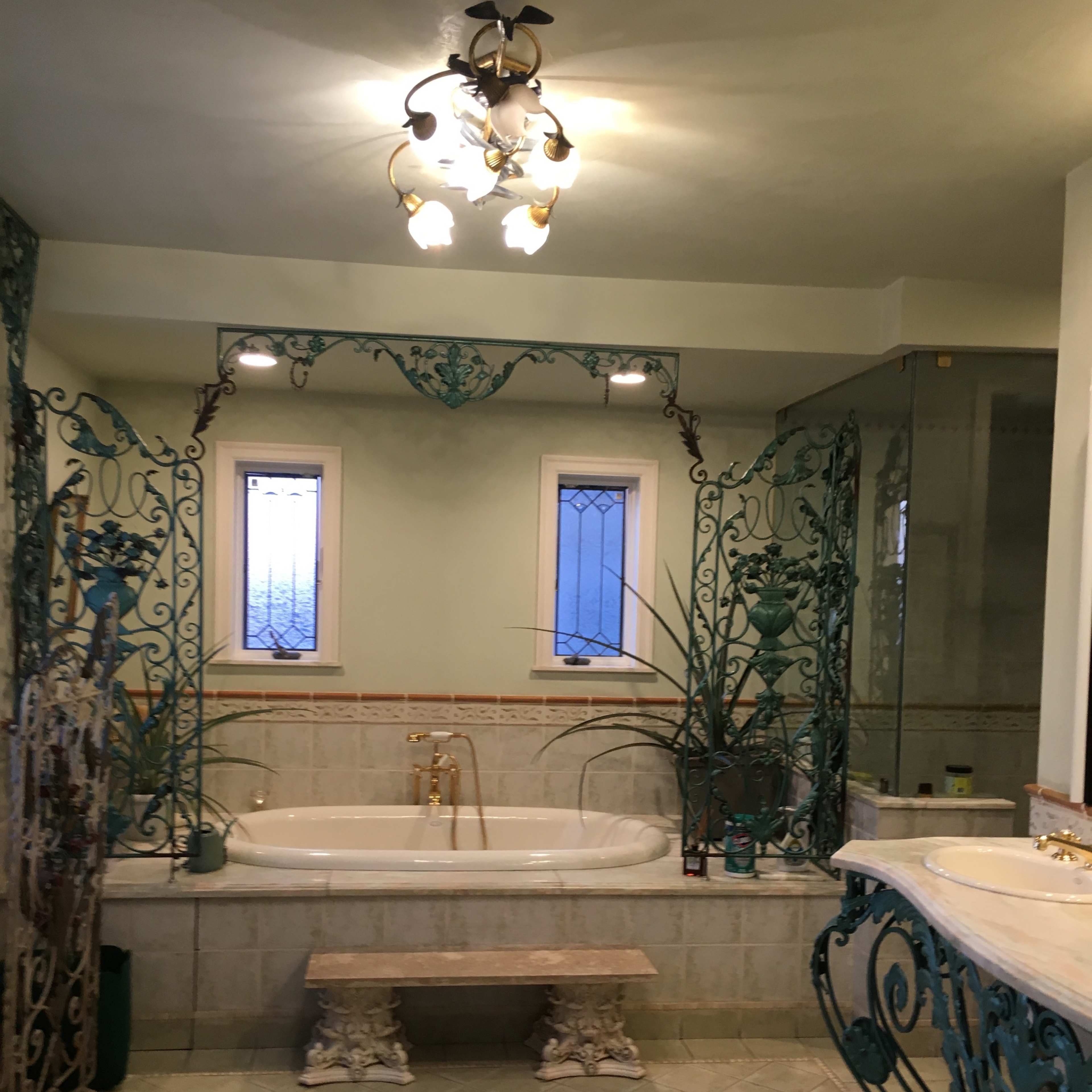 The bathroom features a large freestanding tub surrounded by decorative ironwork, a dual sink vanity, and natural light coming through two windows.