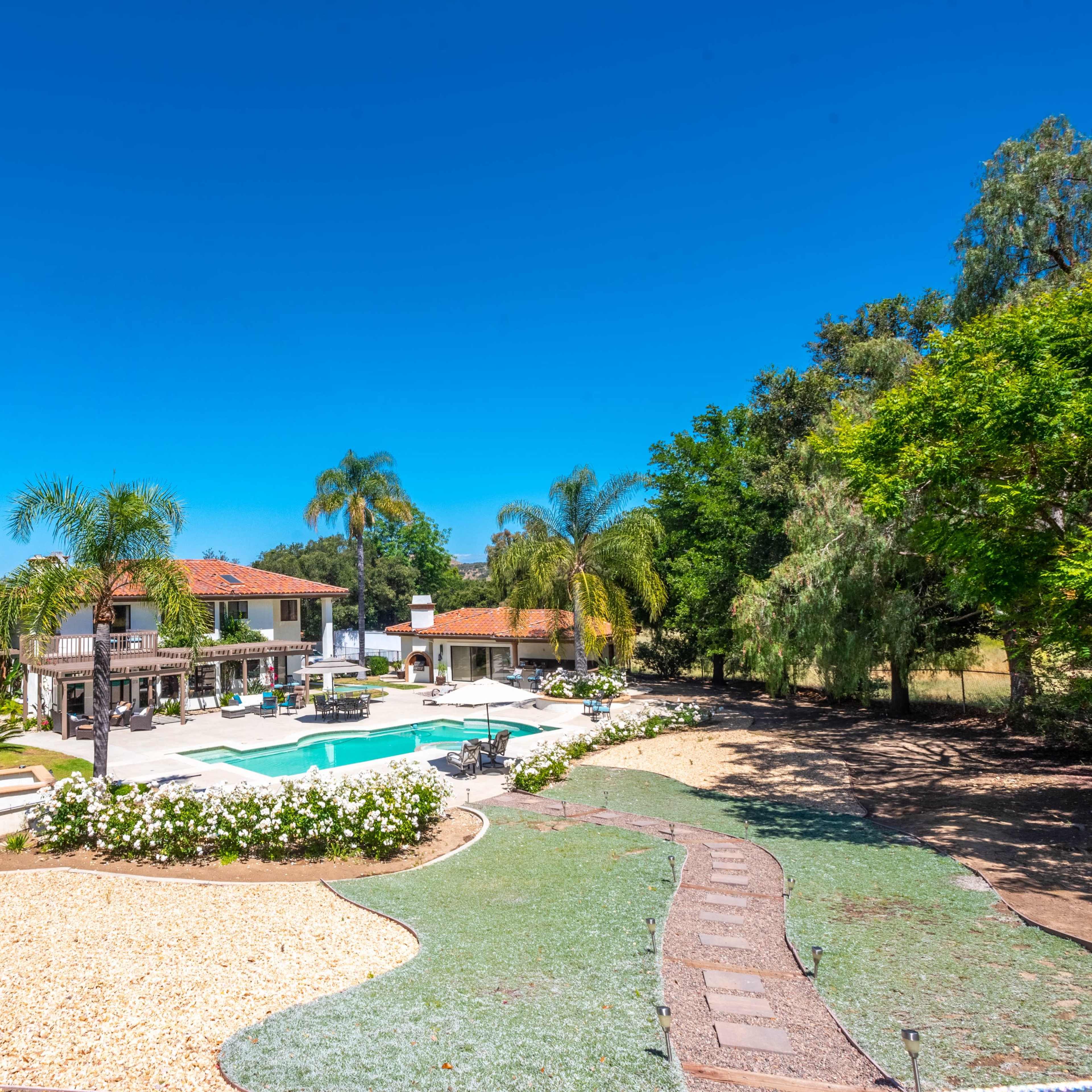 A spacious backyard features a swimming pool surrounded by landscaped gardens and a modern house in the background.