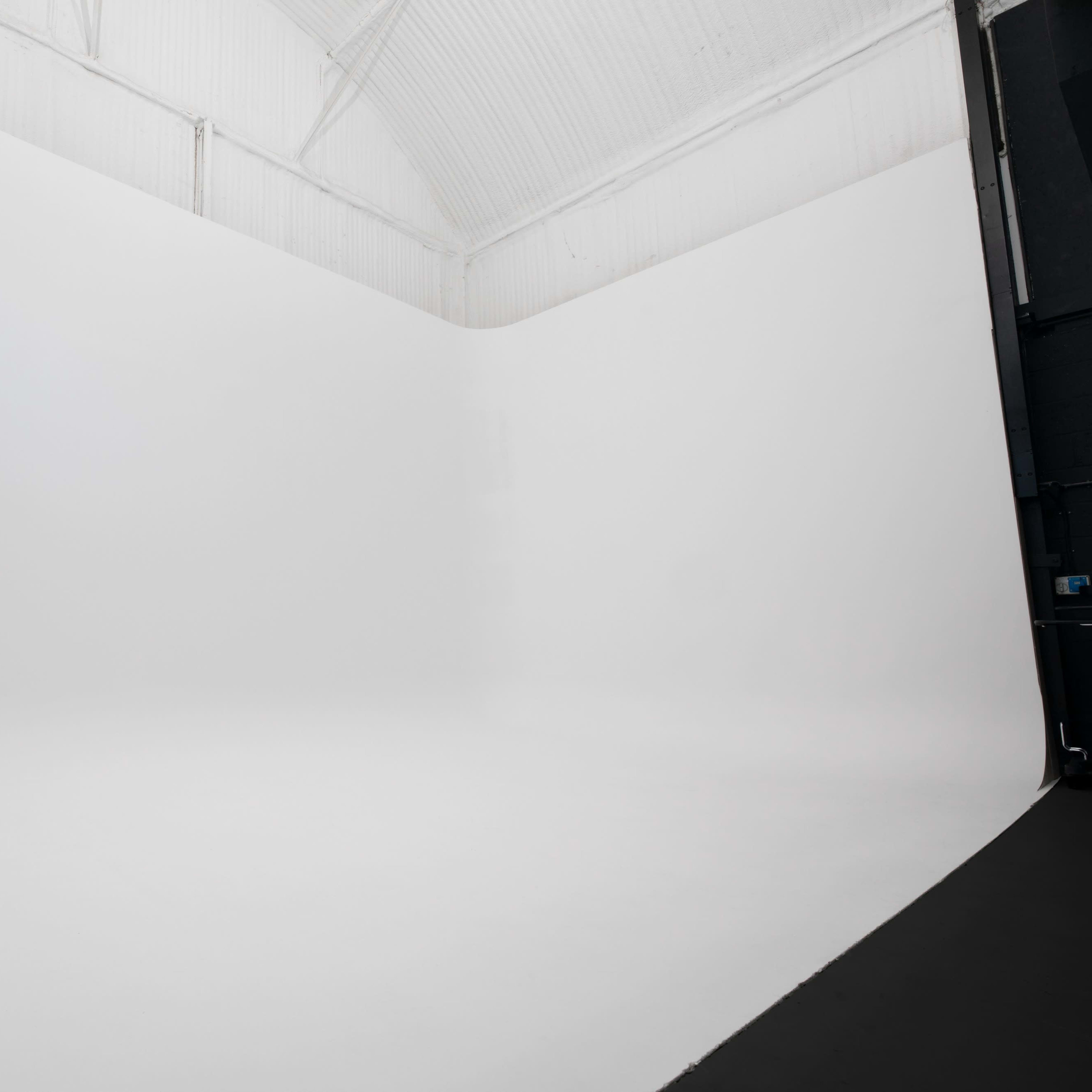 A large, empty studio space with white walls and a seamless white backdrop.
