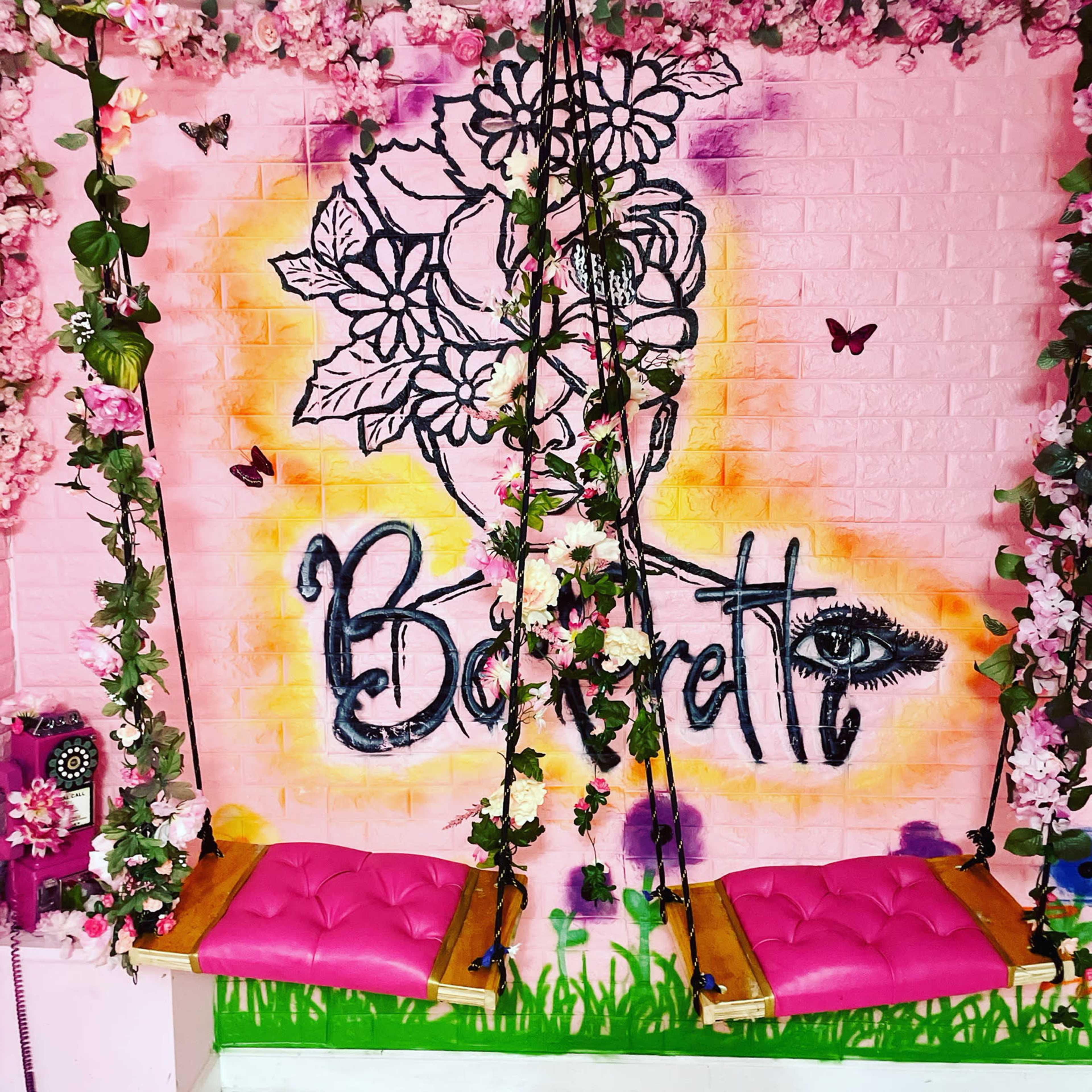 A vibrant room with two swings adorned with floral decorations and a colorful mural of a face surrounded by flowers on the wall.