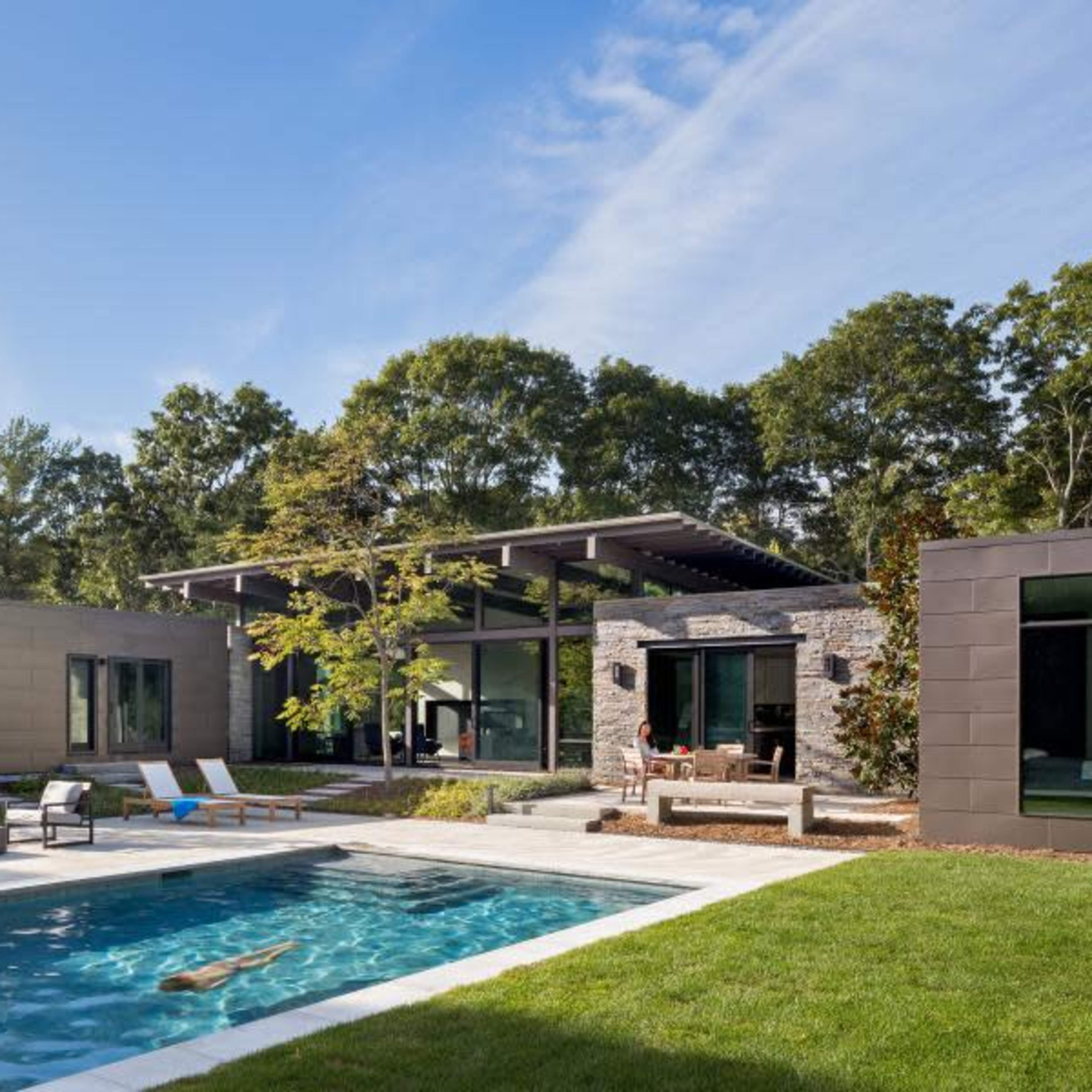 A modern home with a swimming pool surrounded by landscaped grass and trees.