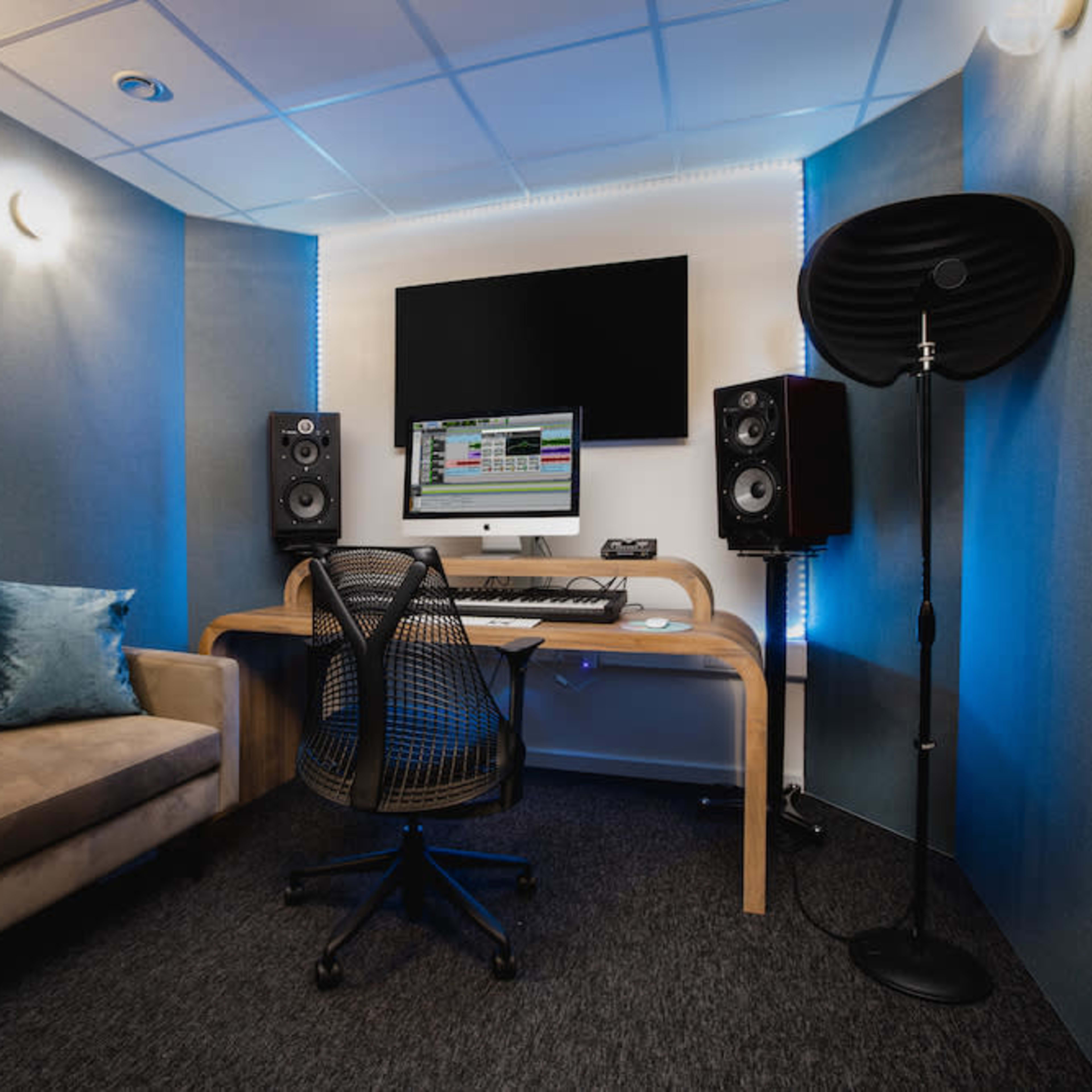 A modern recording studio featuring a computer workstation, studio monitors, and a comfortable couch in a sound-treated environment.