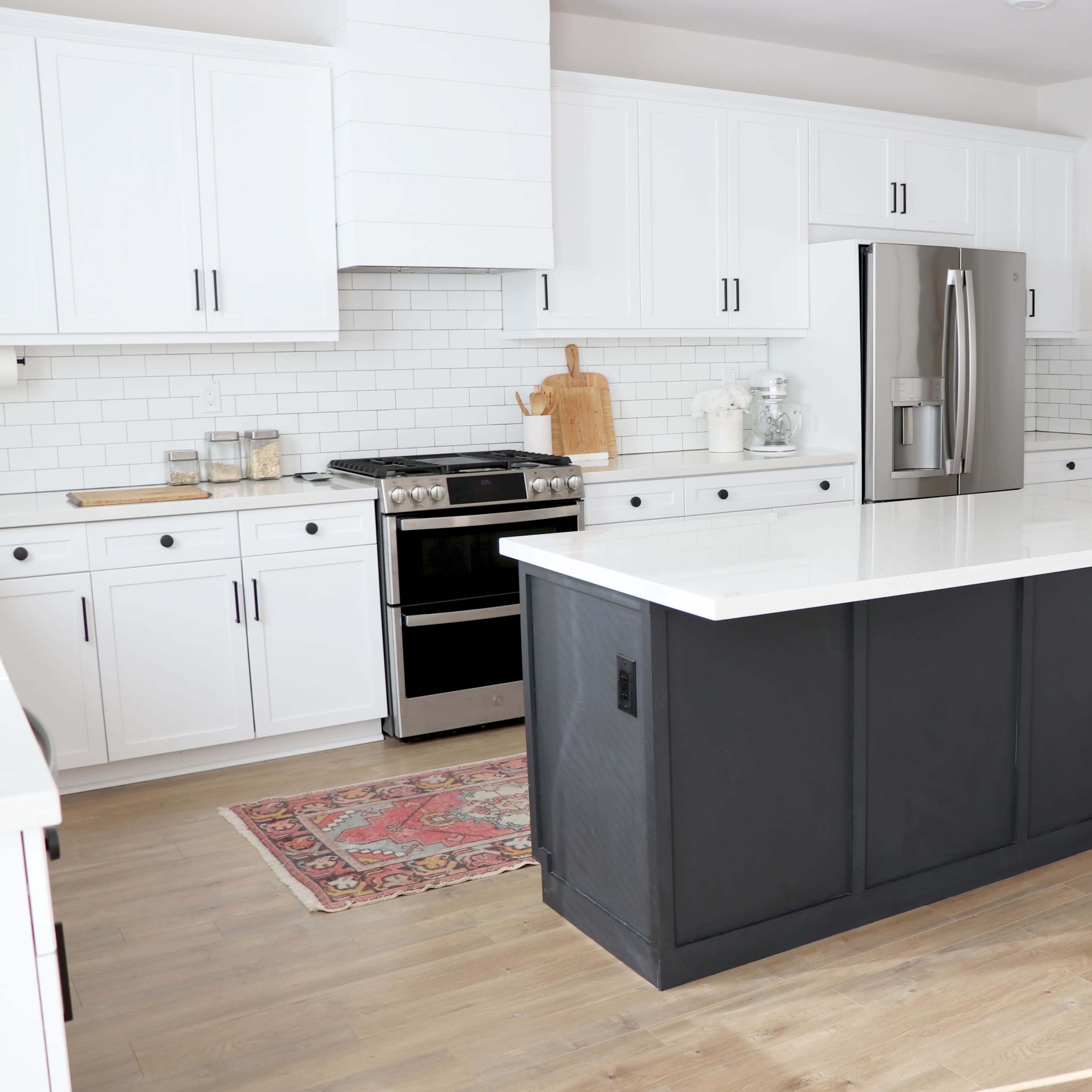 A modern kitchen features white cabinetry, stainless steel appliances, and a dark island with a marble countertop.