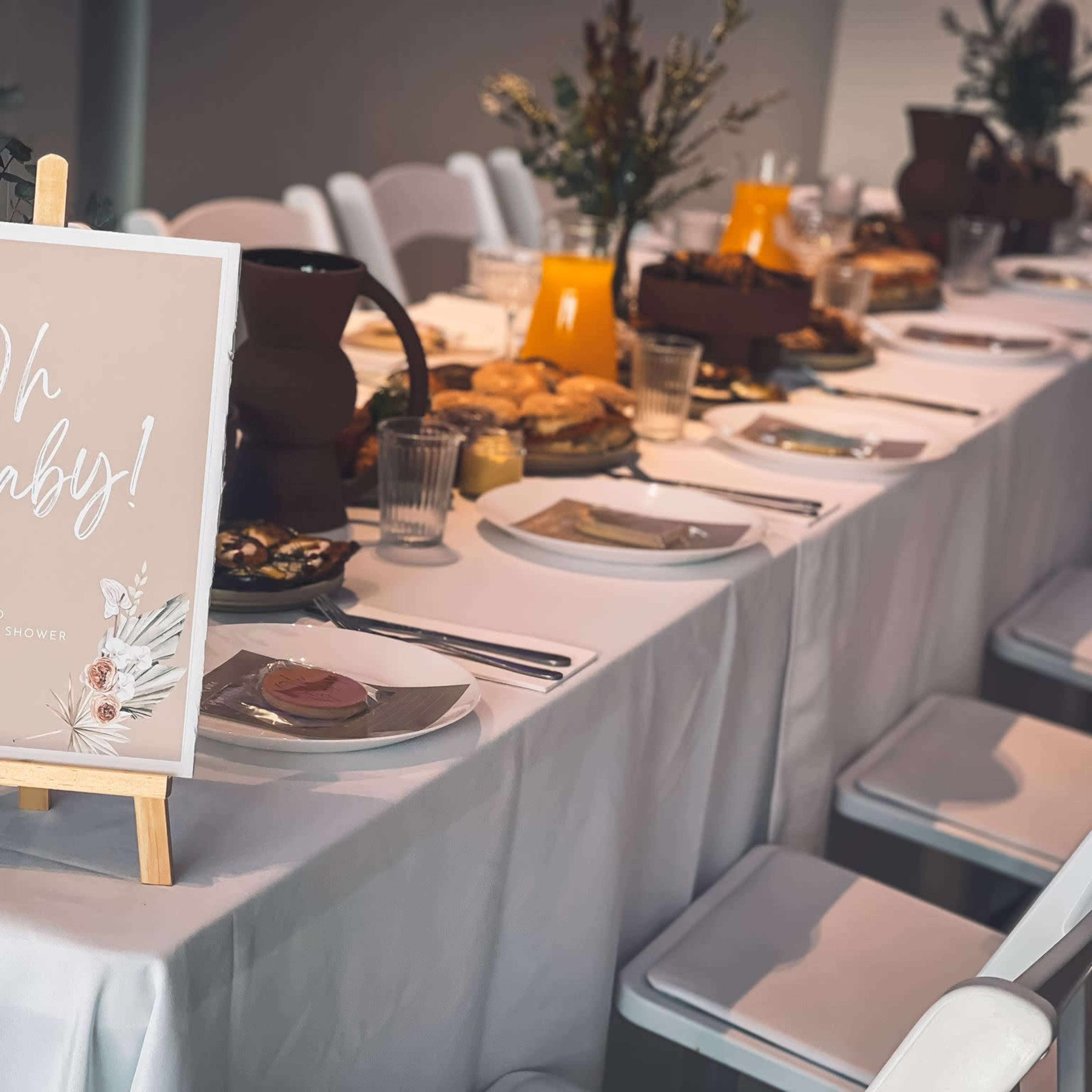 A long, elegantly set table with plates, drinks, and a decorative sign reading "Oh Baby! Welcome to Mali's Baby Shower."