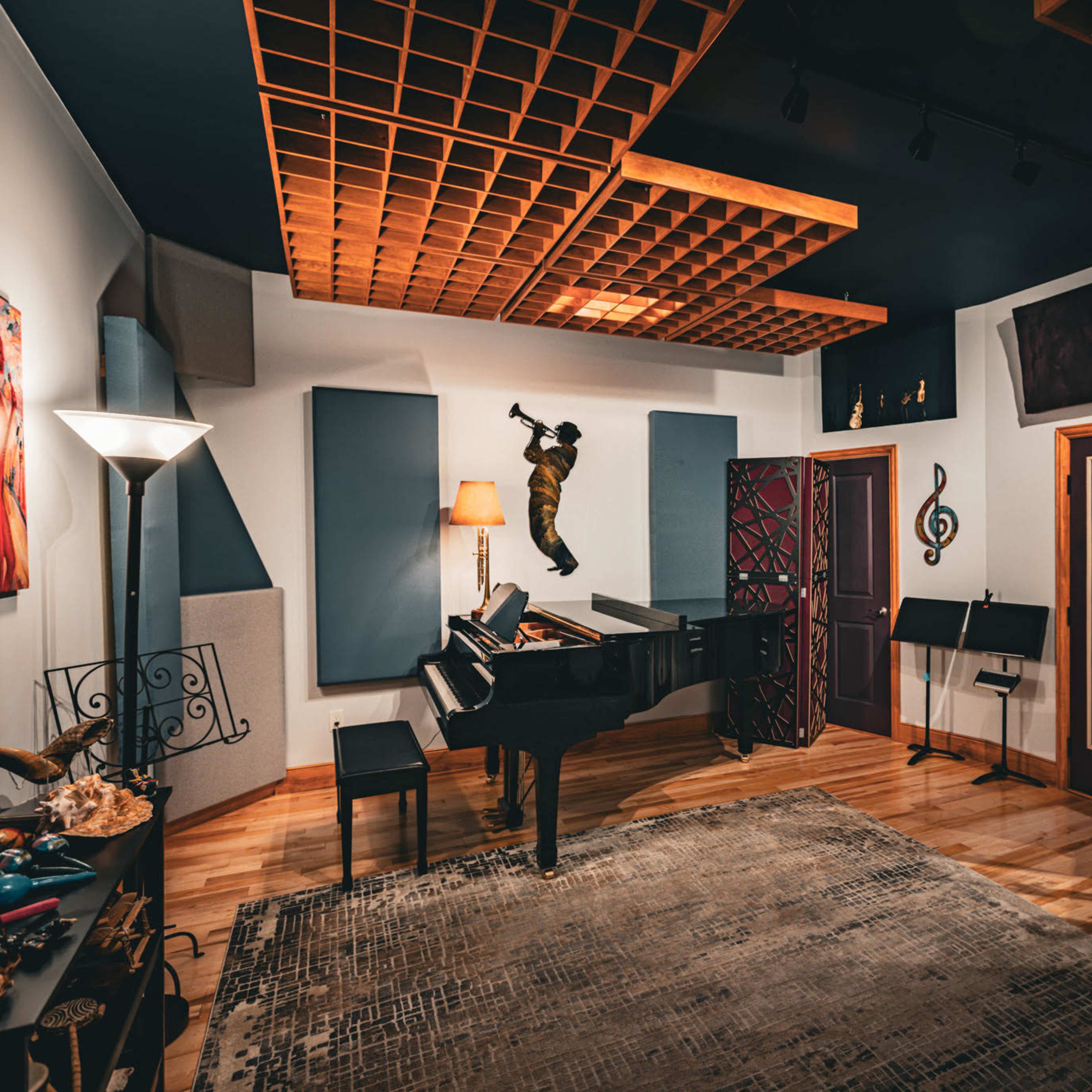 A well-equipped music studio features a grand piano, music stands, and soundproofing elements, with artistic décor on the walls.