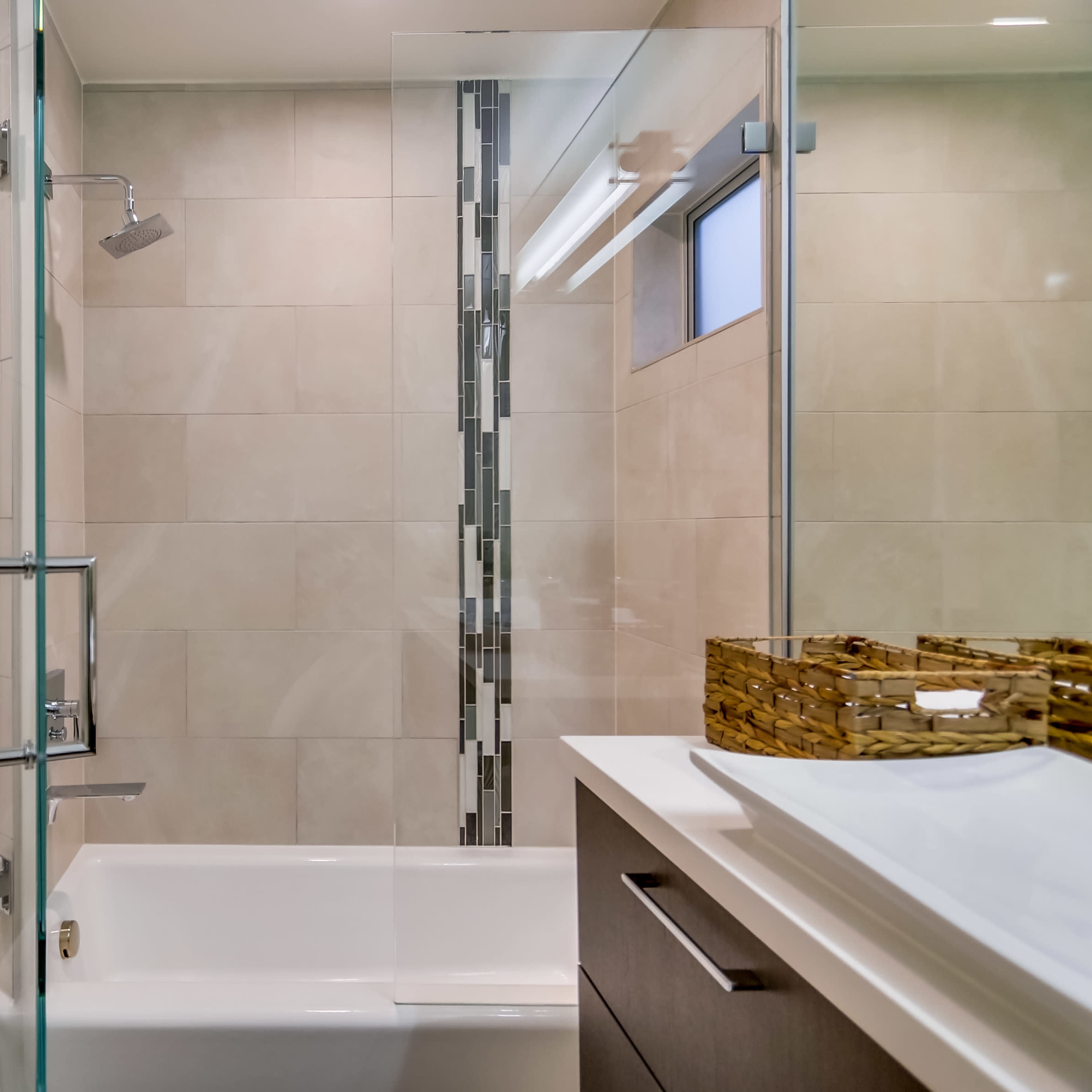 A modern bathroom with a glass shower enclosure, a white bathtub, and a sink with a wooden storage unit.