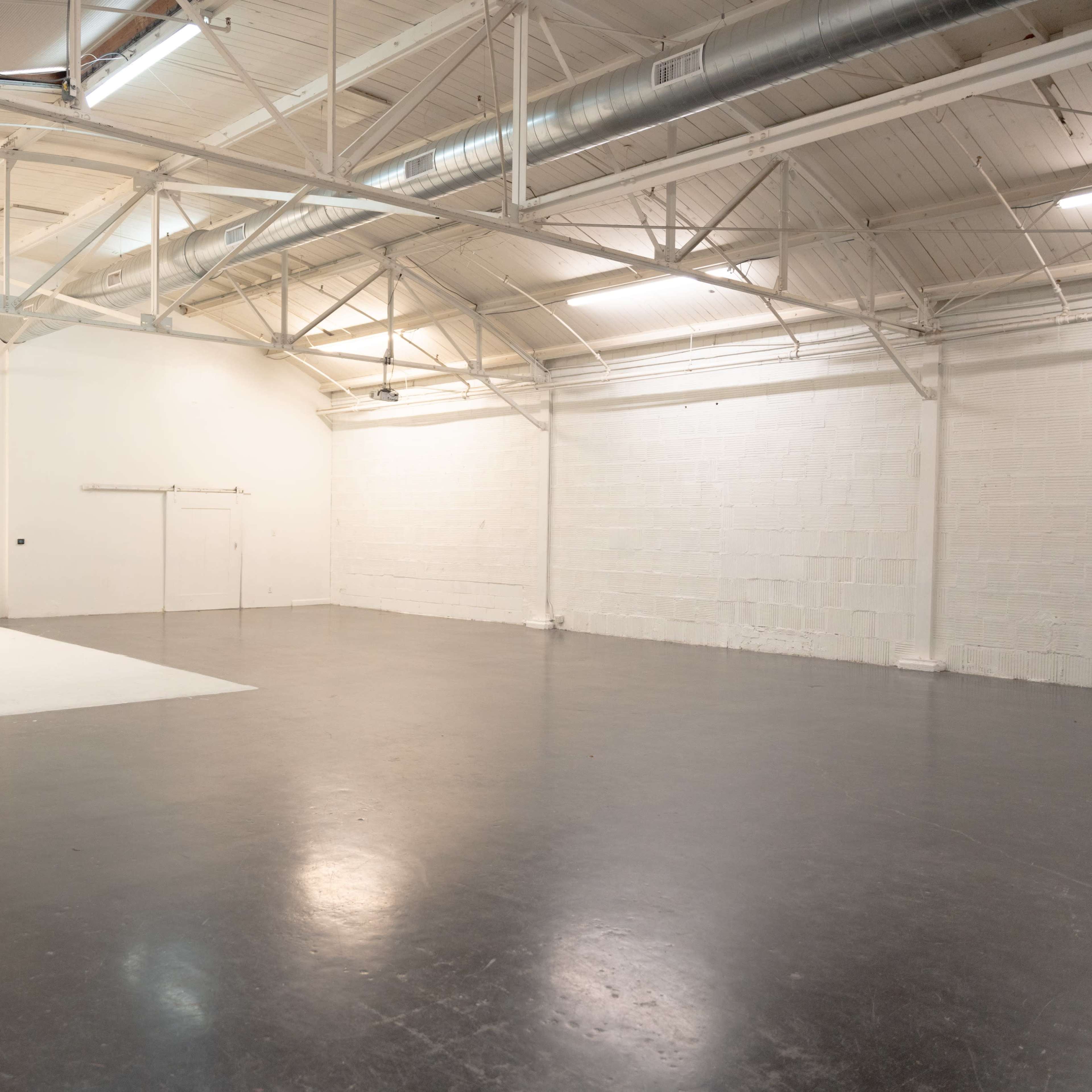 A spacious, empty studio with a white backdrop and a polished concrete floor.