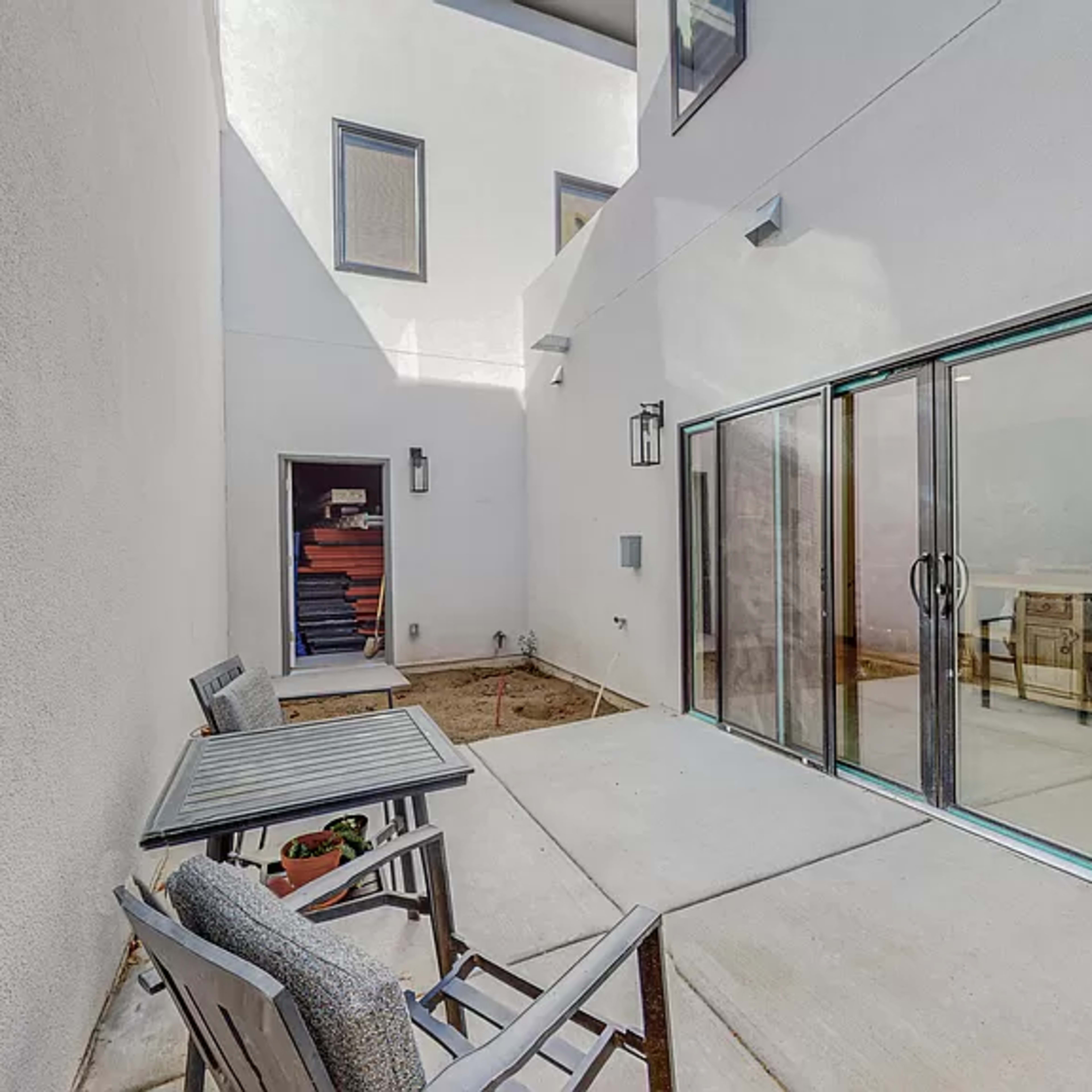A small outdoor patio area with a table and chairs, enclosed by white walls and glass sliding doors.