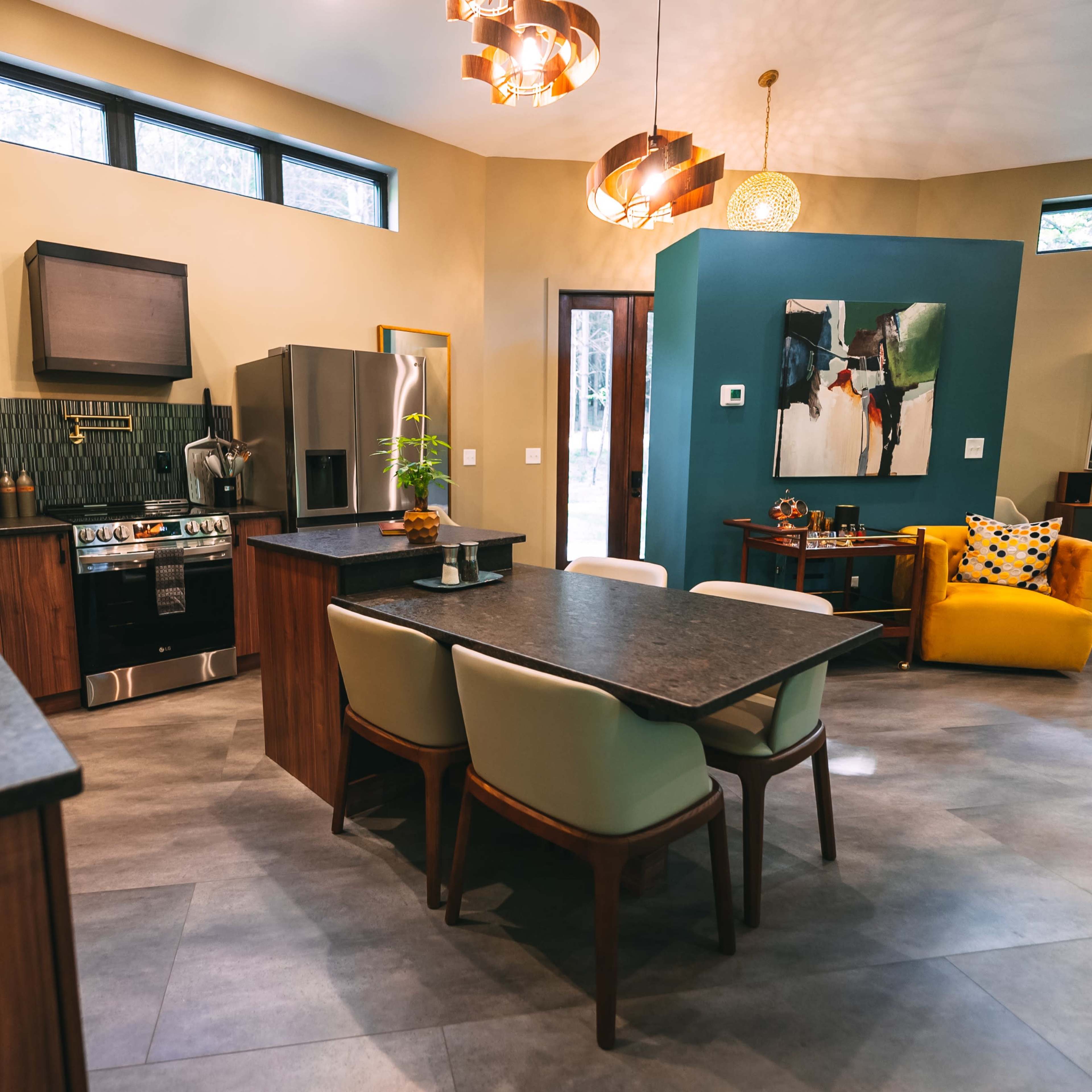 A modern kitchen and dining area featuring wooden cabinets, a stainless steel refrigerator, a dining table with upholstered chairs, and a bright yellow accent chair in a corner.