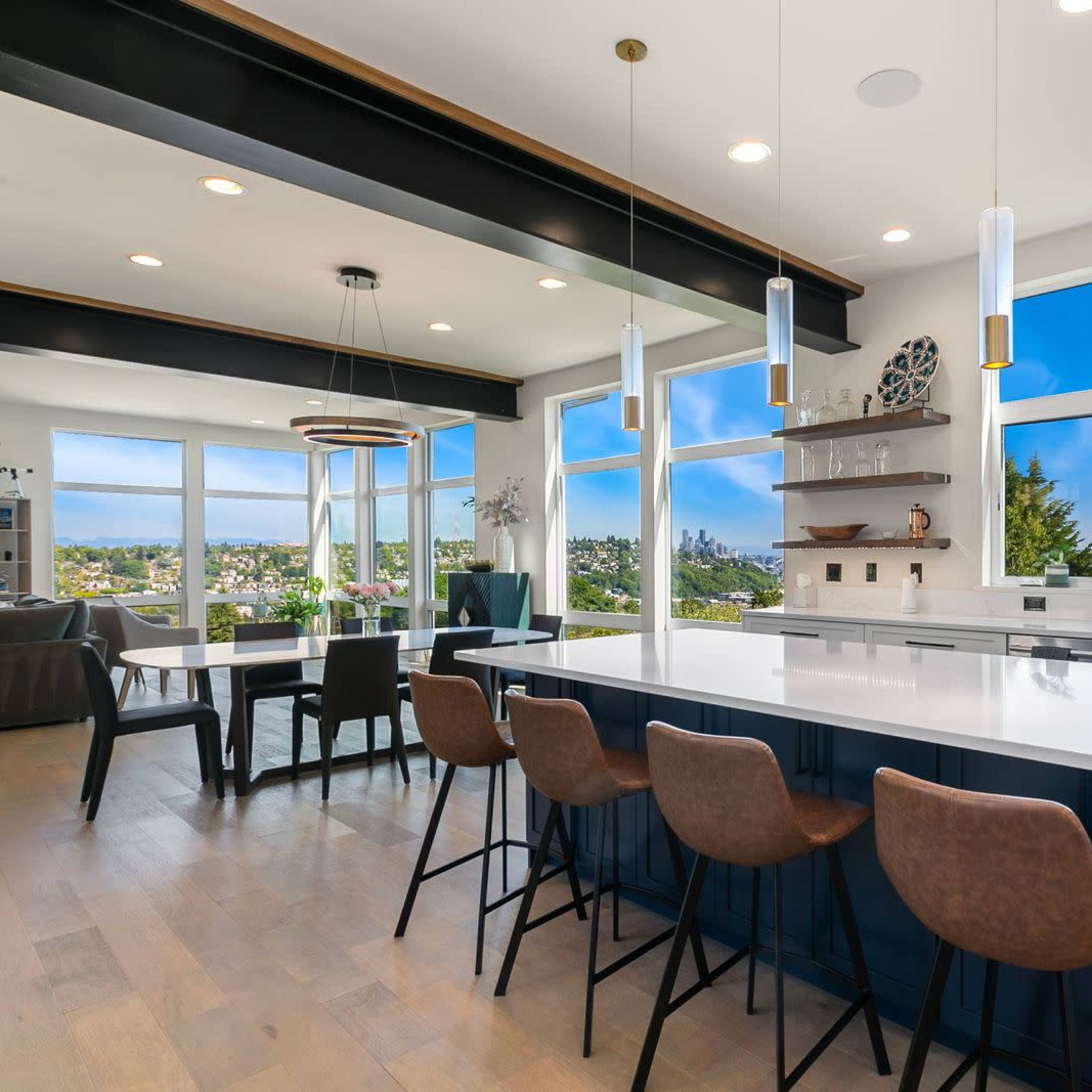 A modern kitchen features an island with seating, large windows showcasing a scenic view, and sleek cabinetry.