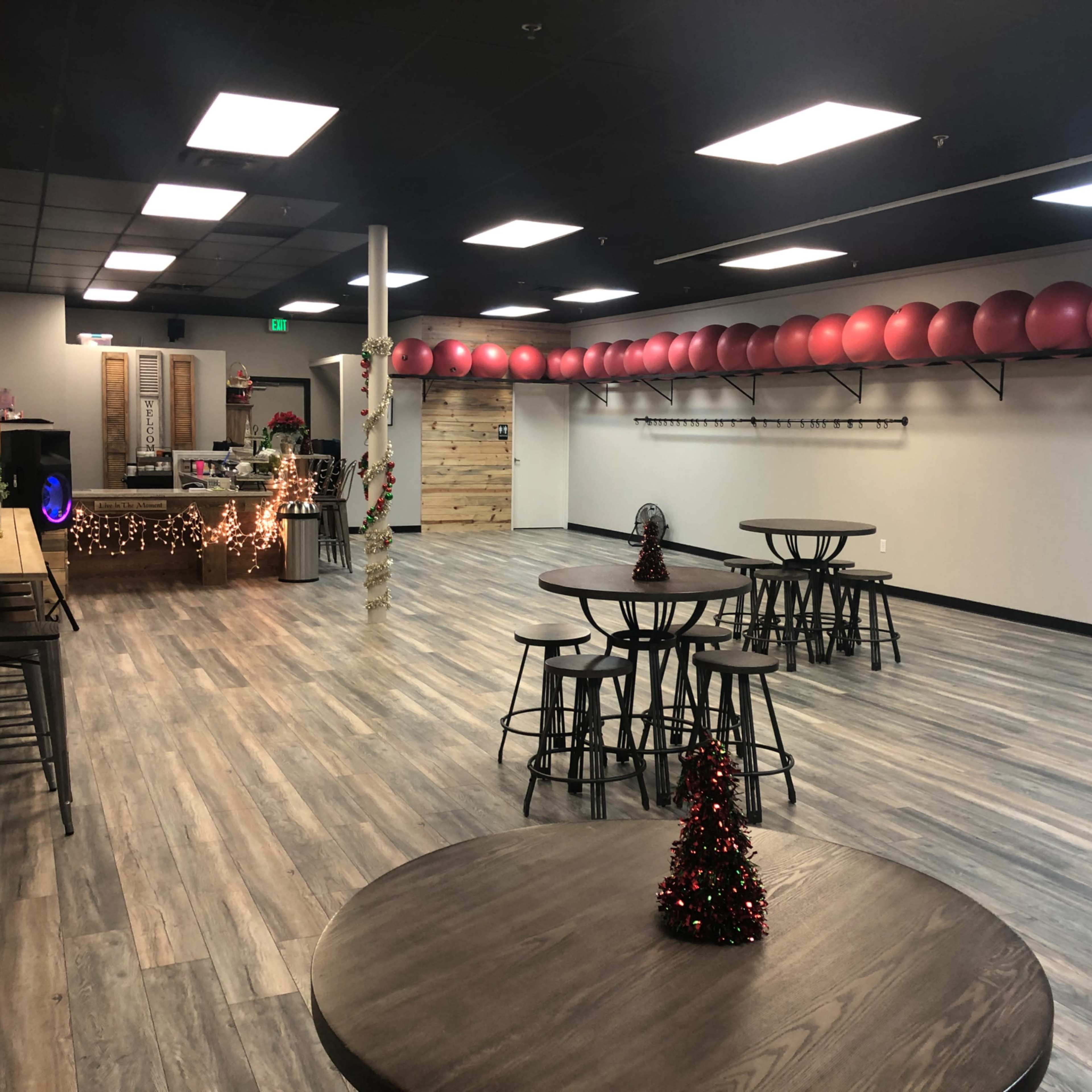 A spacious fitness studio with wooden flooring, several round tables, and a row of exercise balls along the back wall.