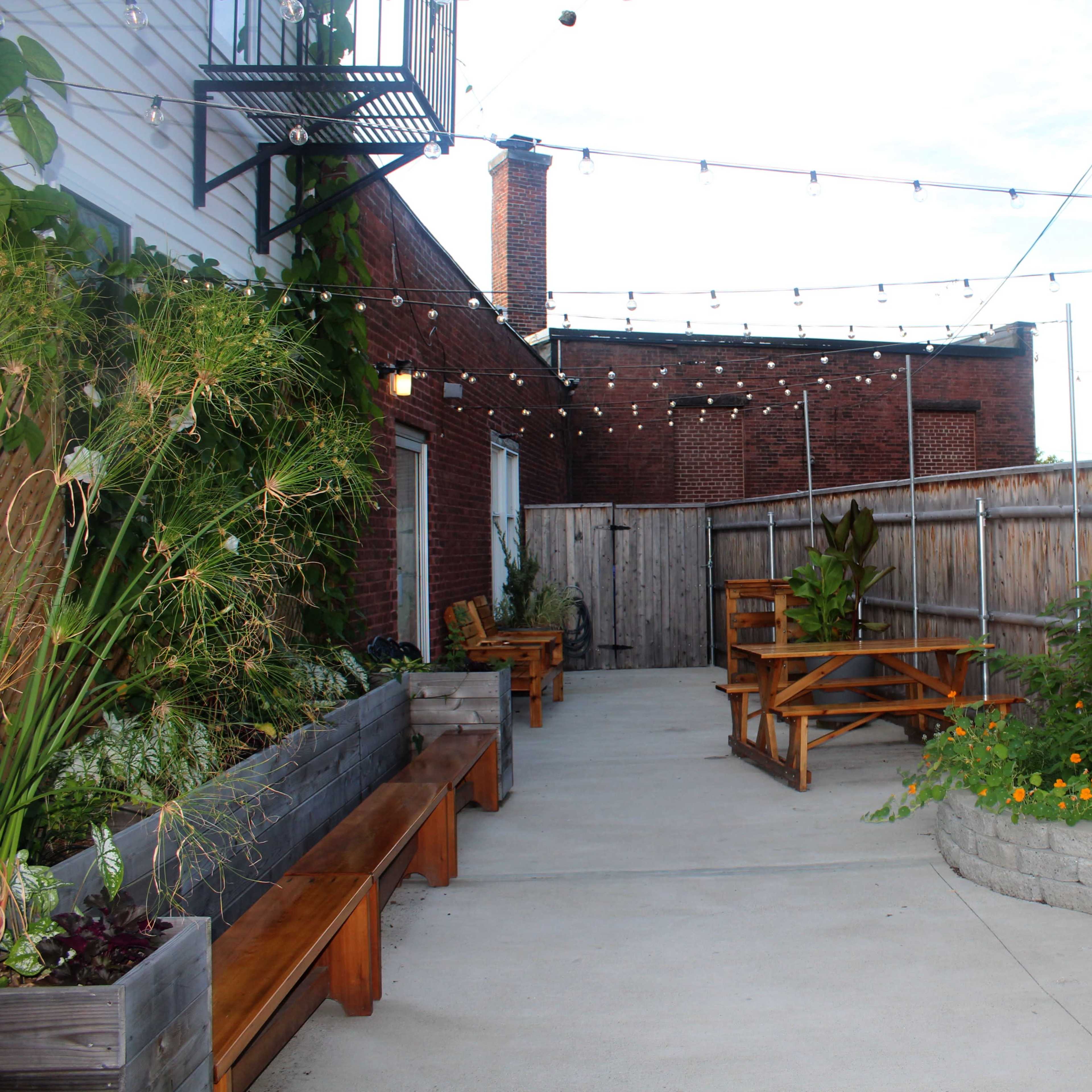 A small outdoor seating area with wooden picnic tables and benches, surrounded by a wooden fence and plants.