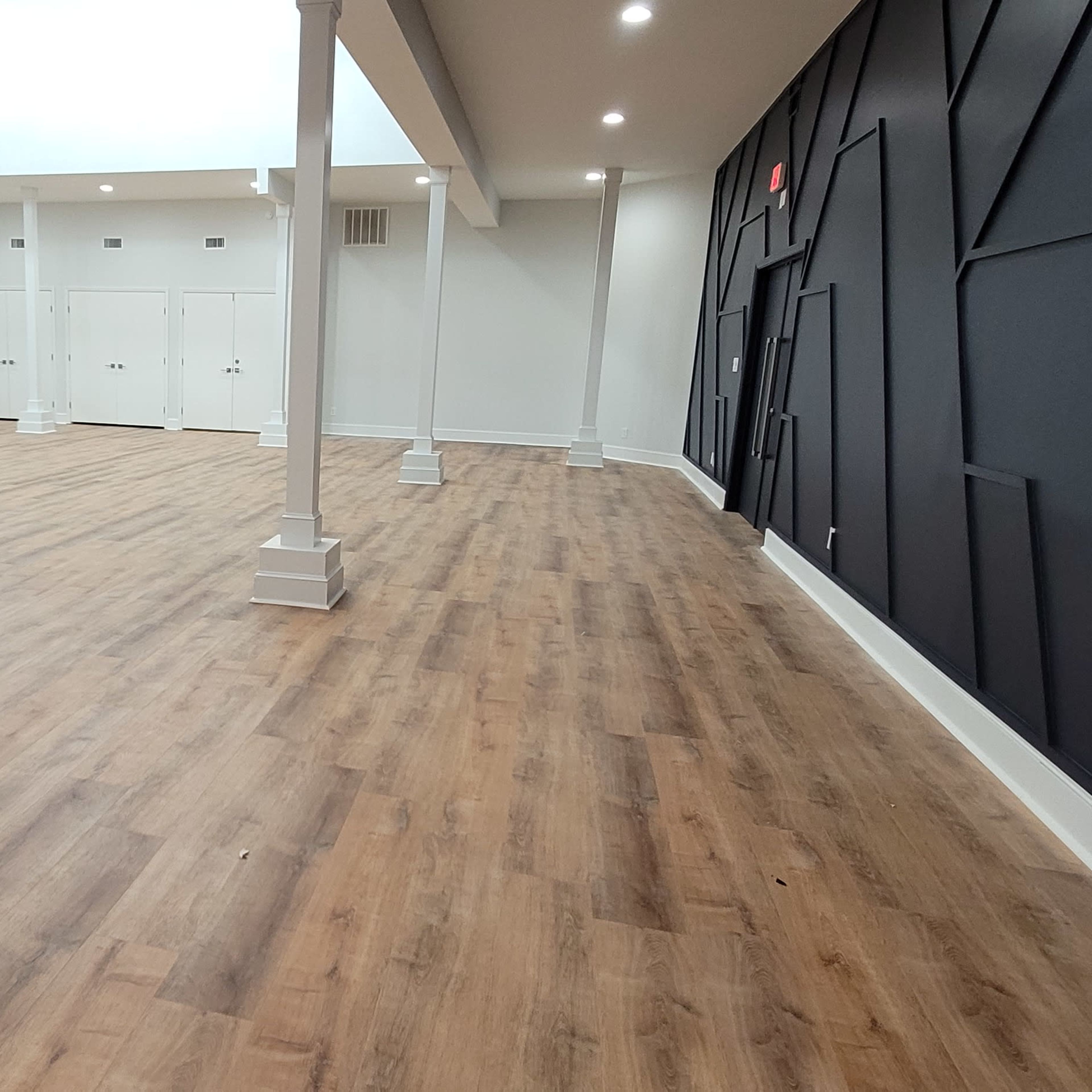 An expansive interior space features wooden flooring, white columns, and a dark accent wall with geometric designs.